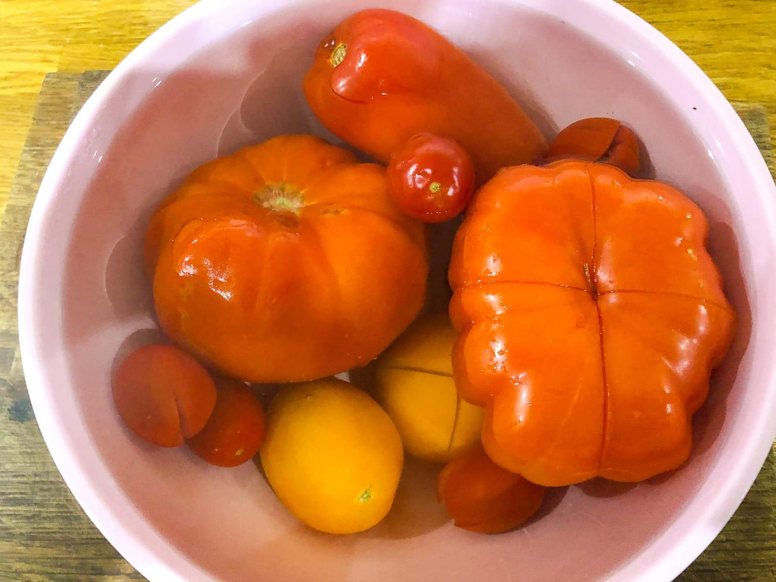 A selection of fresh red and yellow tomatoes with the bottoms sliced slightly to prepare for skinning.