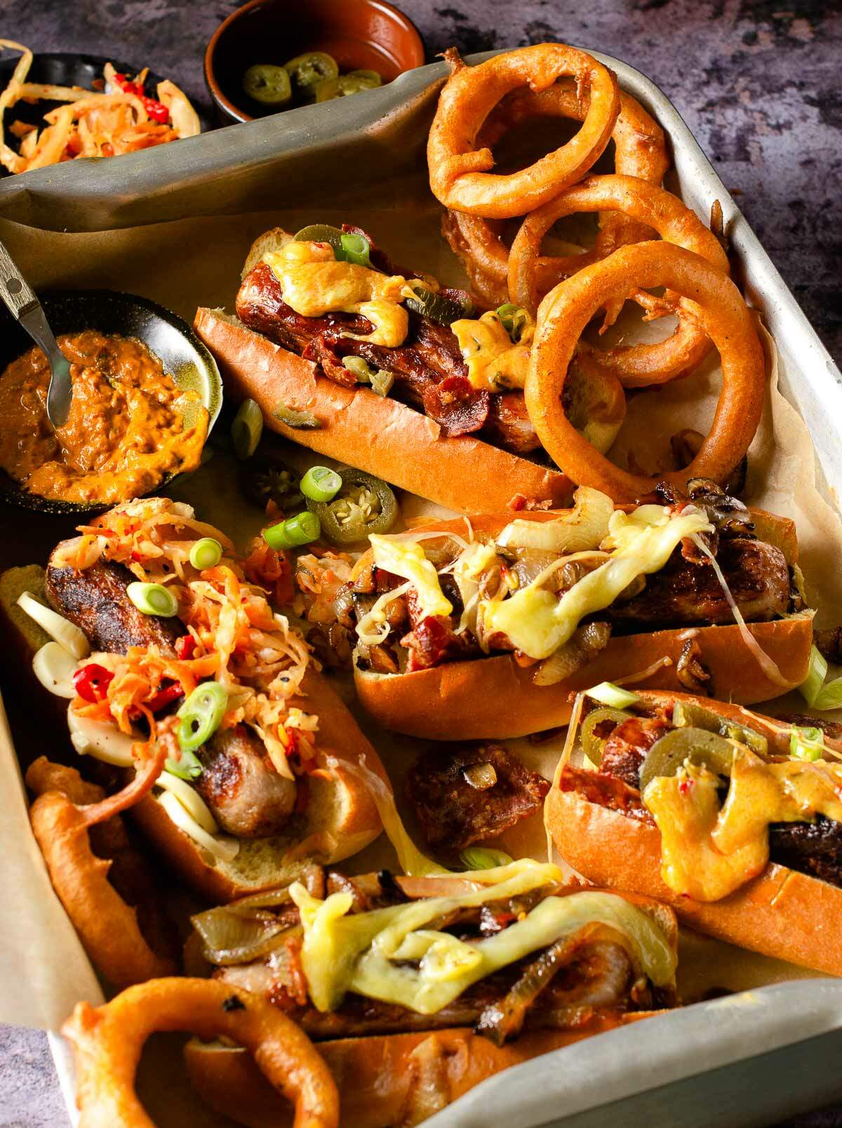 Hot dogs, loaded with toppings in a metal tray.