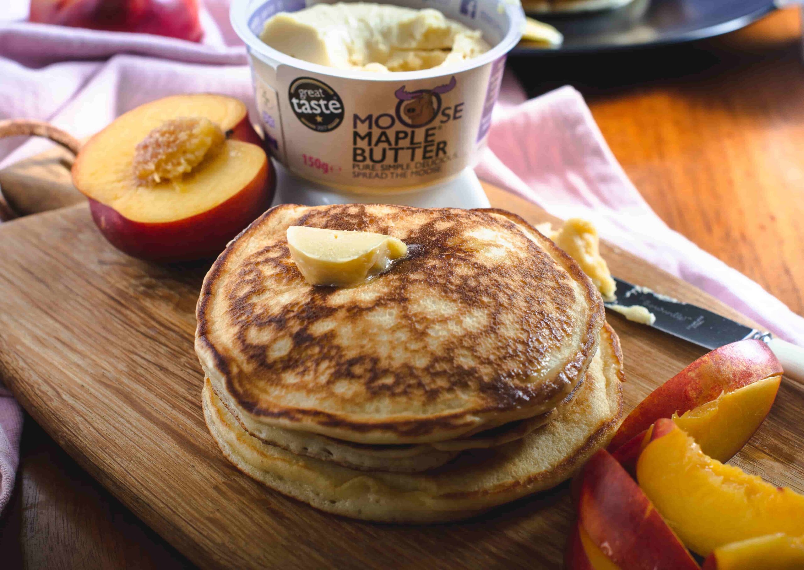 Pancakes served with fresh necatines and Moose maple Butter on a wooden breakfast table.