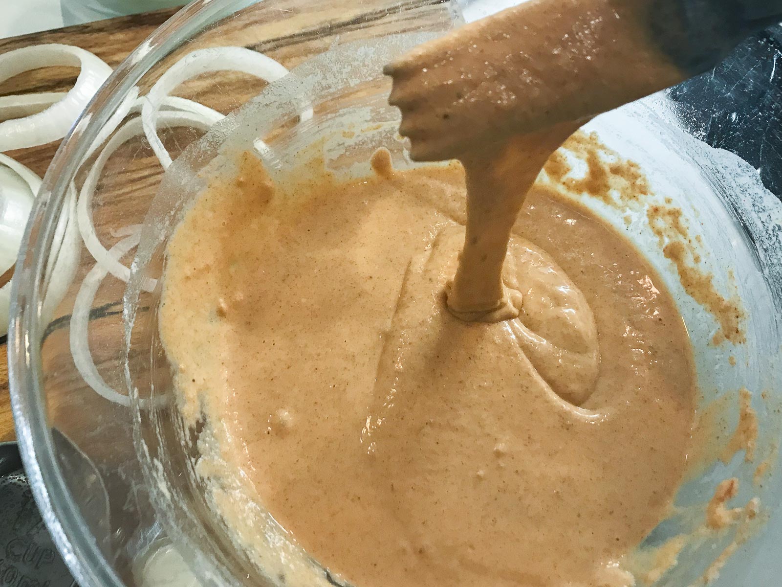 Batter for preparing onion rings in a glass bowl and raw onions ready to be made.