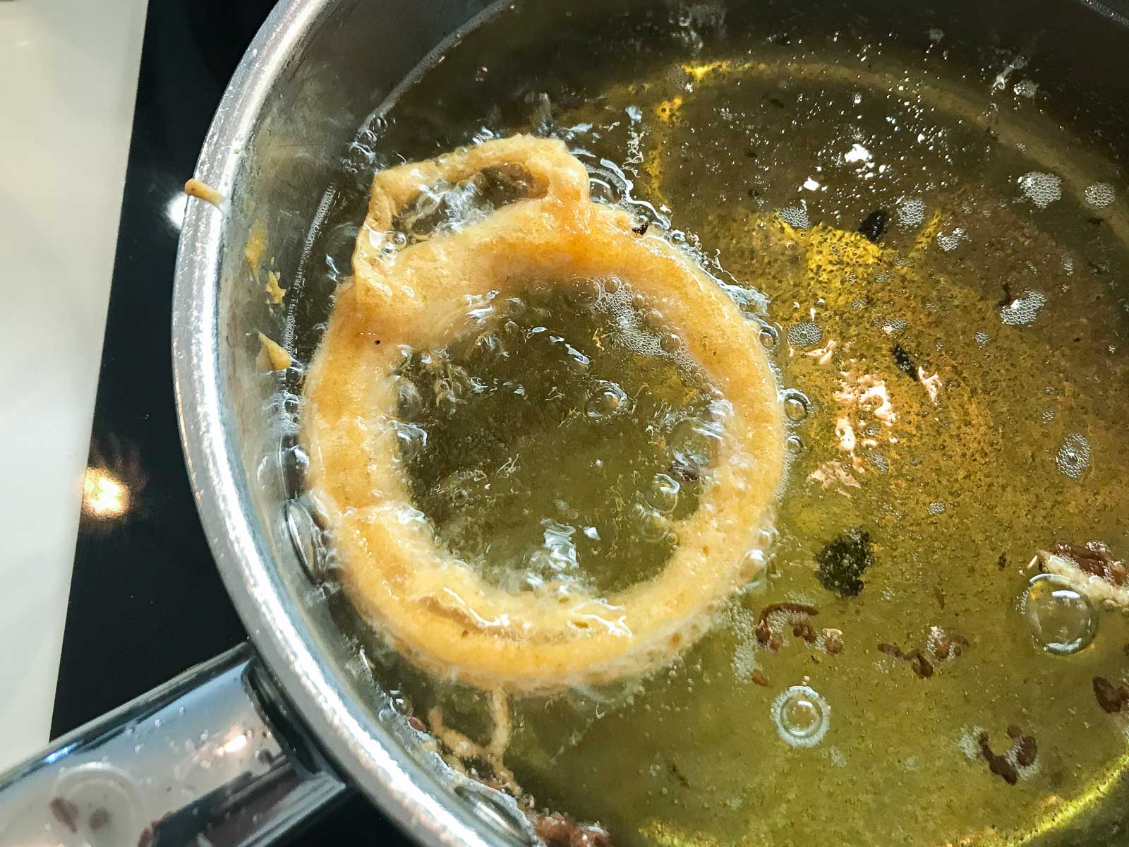 An onion ring frying in oil in a pan.