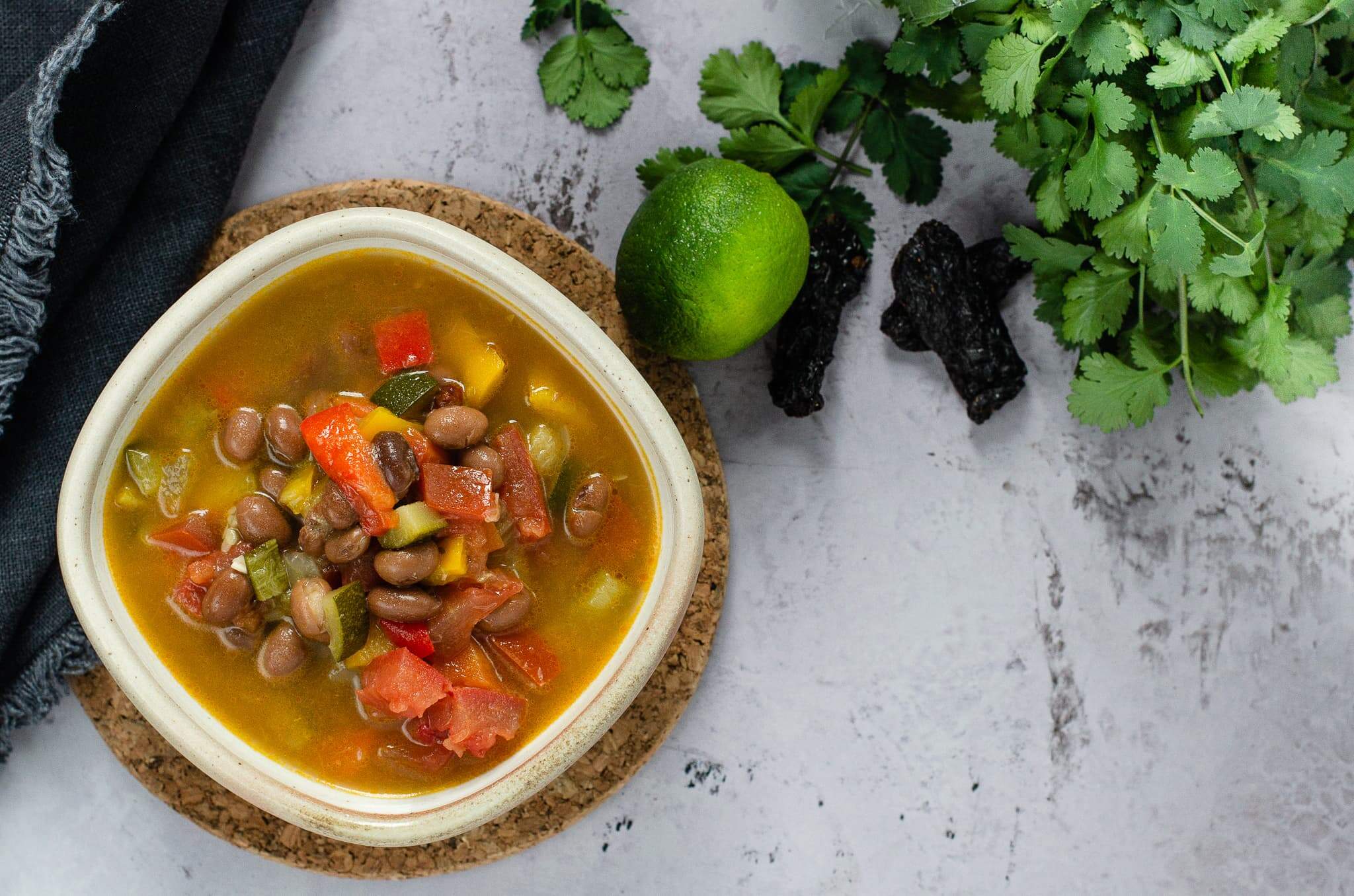 Bowl of spicy bean and vegetable soup on a marble effect backdrop with a lime and coriander in the back