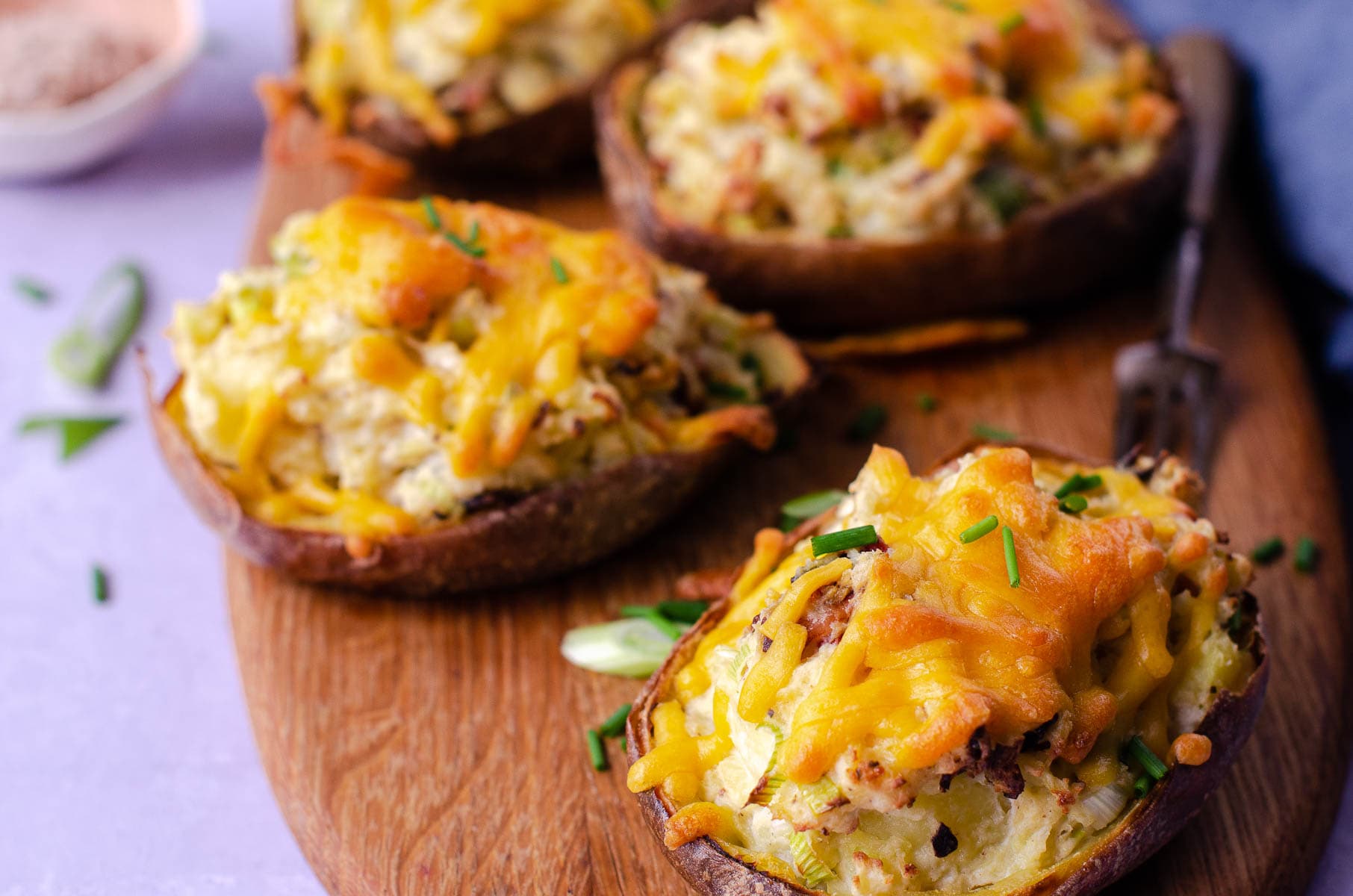 Twice baked potatoes loaded with cheese, onion and bacon served on a wooden chopping board and scattered with spring onions.
