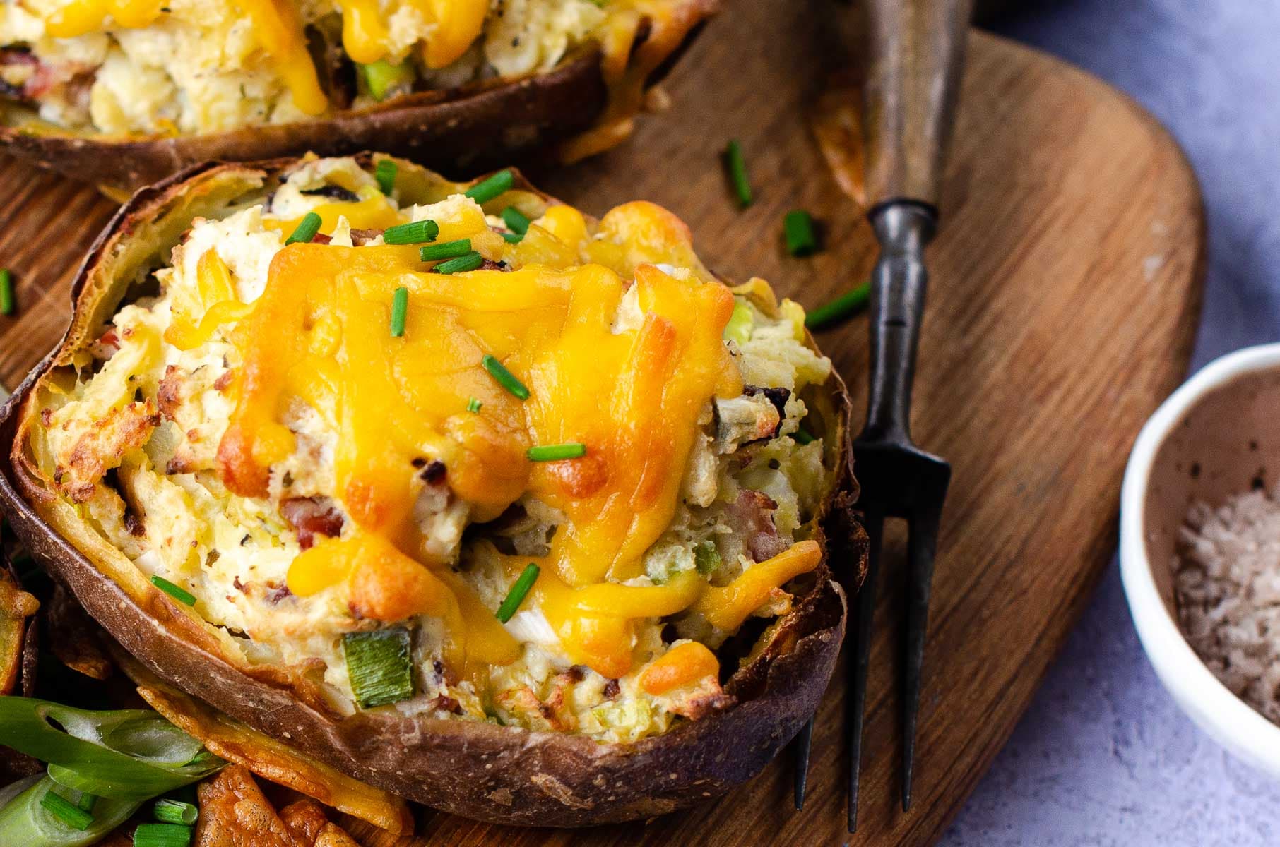 Close up of a twice baked and filled potato skin topped with cheese.