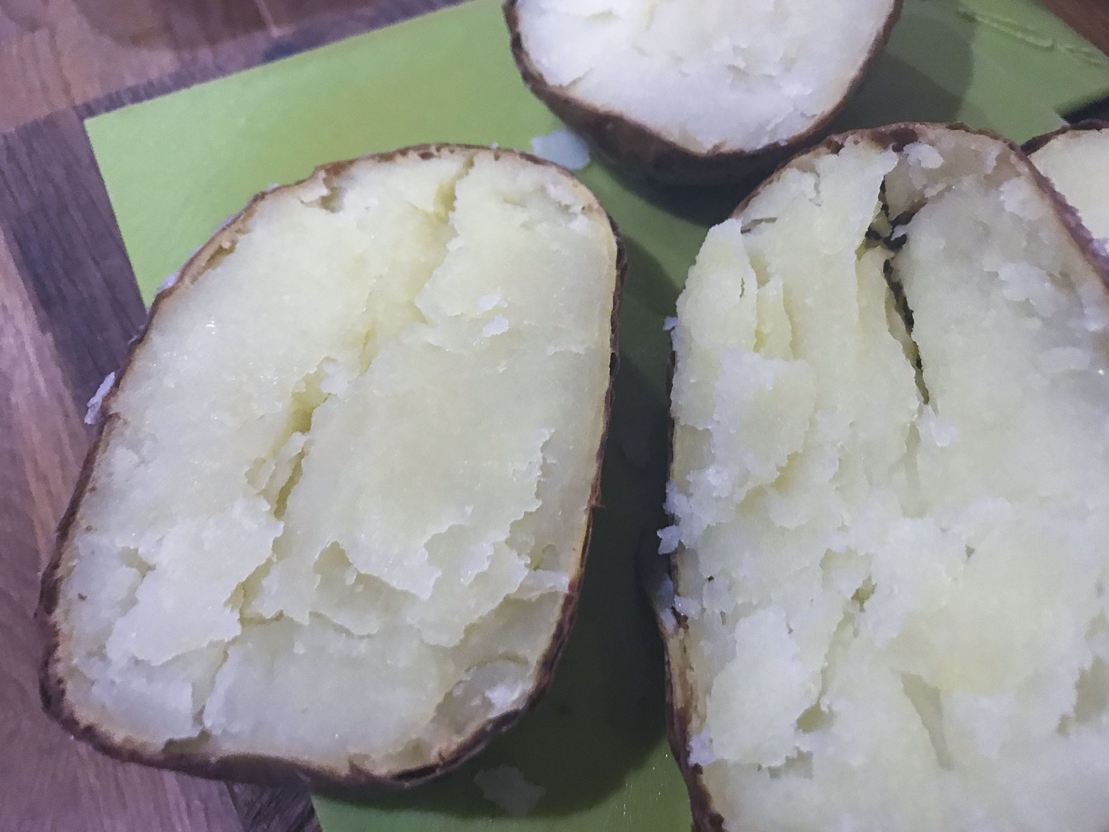 Baked potatoes sliced in half from the oven on a wooden chopping board.