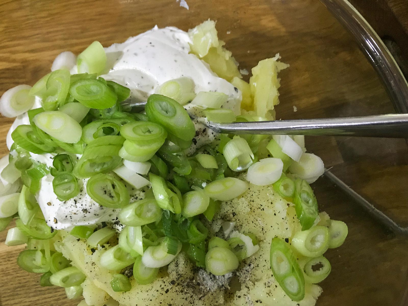 Mashed potato being mixed with spring onions, soft cheese, salt & pepper.