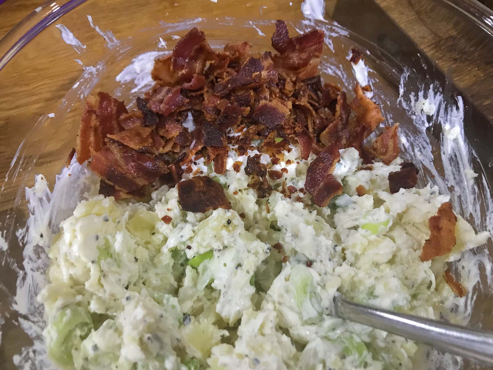 Mashed potato being mixed with spring onions, soft cheese, salt & pepper and crisp diced bacon added.