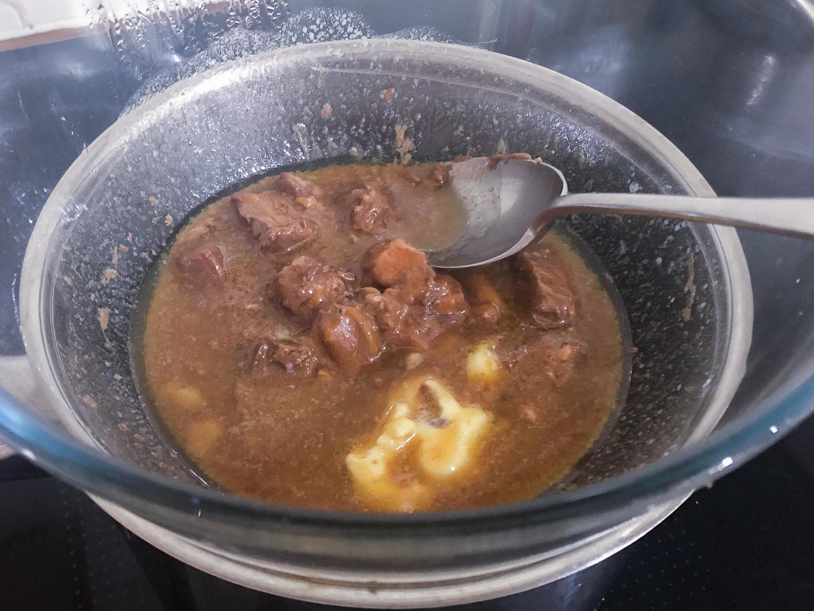 A glass bowl sitting over a pan of simmering water with butter and pieces of mars bars melting inside.