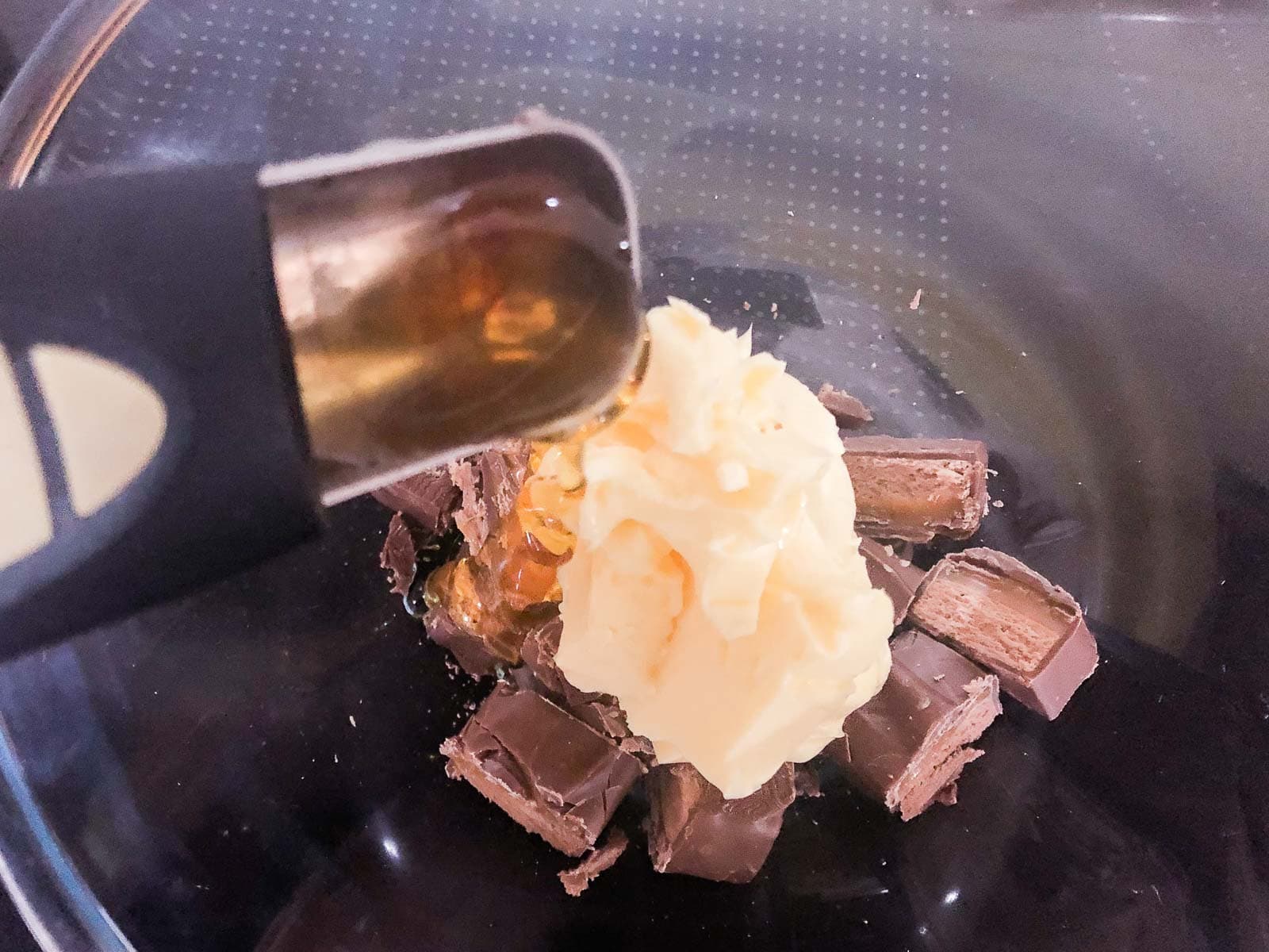 A glass bowl over a pan of simmering water containing mars bars cut into pieces, some butter and a measuring spoon about to add some golden syrup.