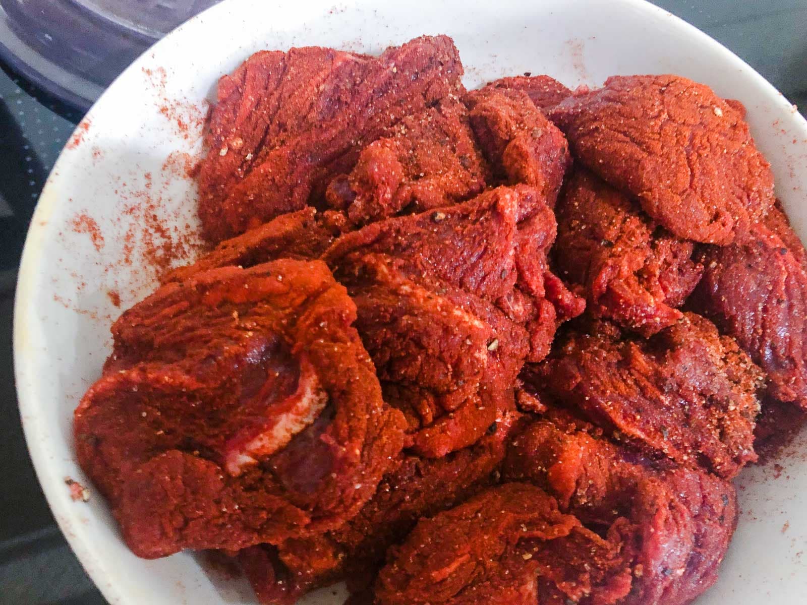 Diced beef tossed in a paprika spice mix sitting in a white bowl about to be cooked before being added to a casserole.