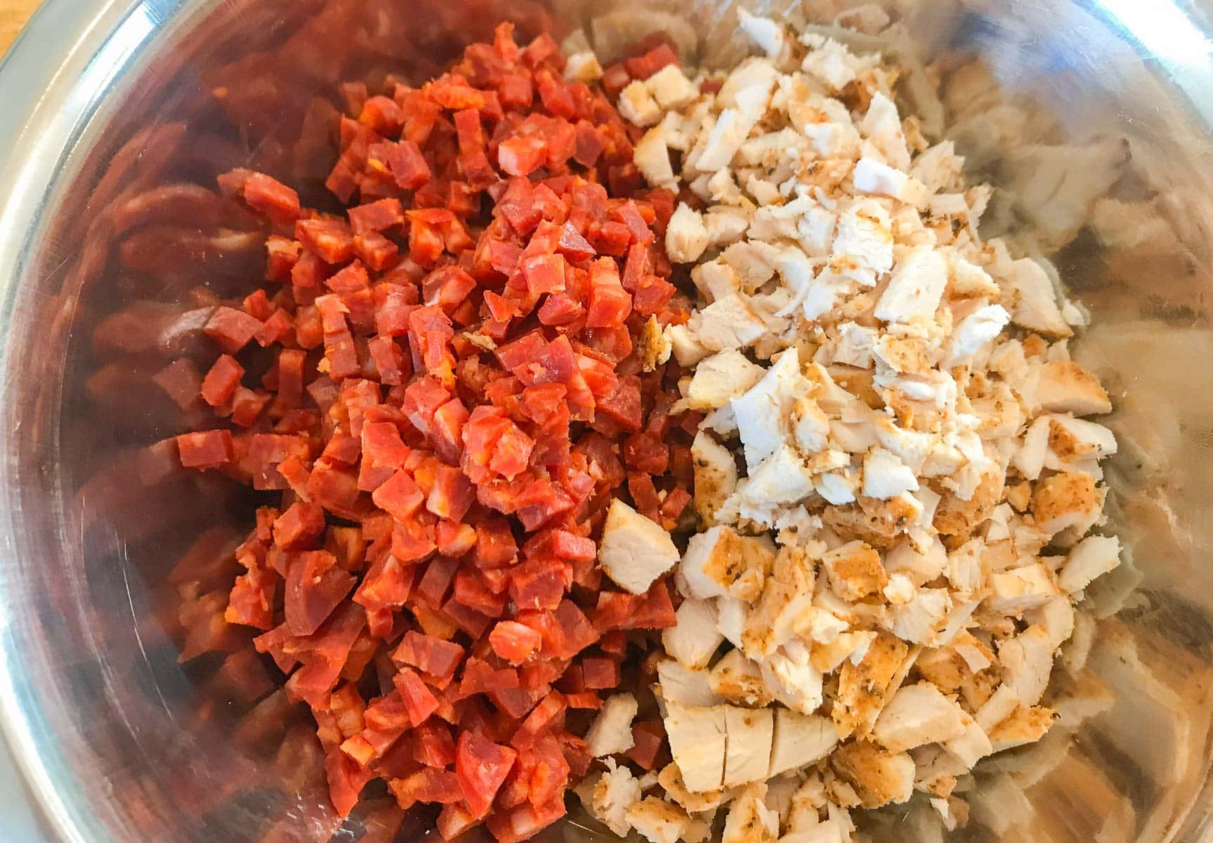 Diced chorizo and diced cooked chicken in a metal bowl.