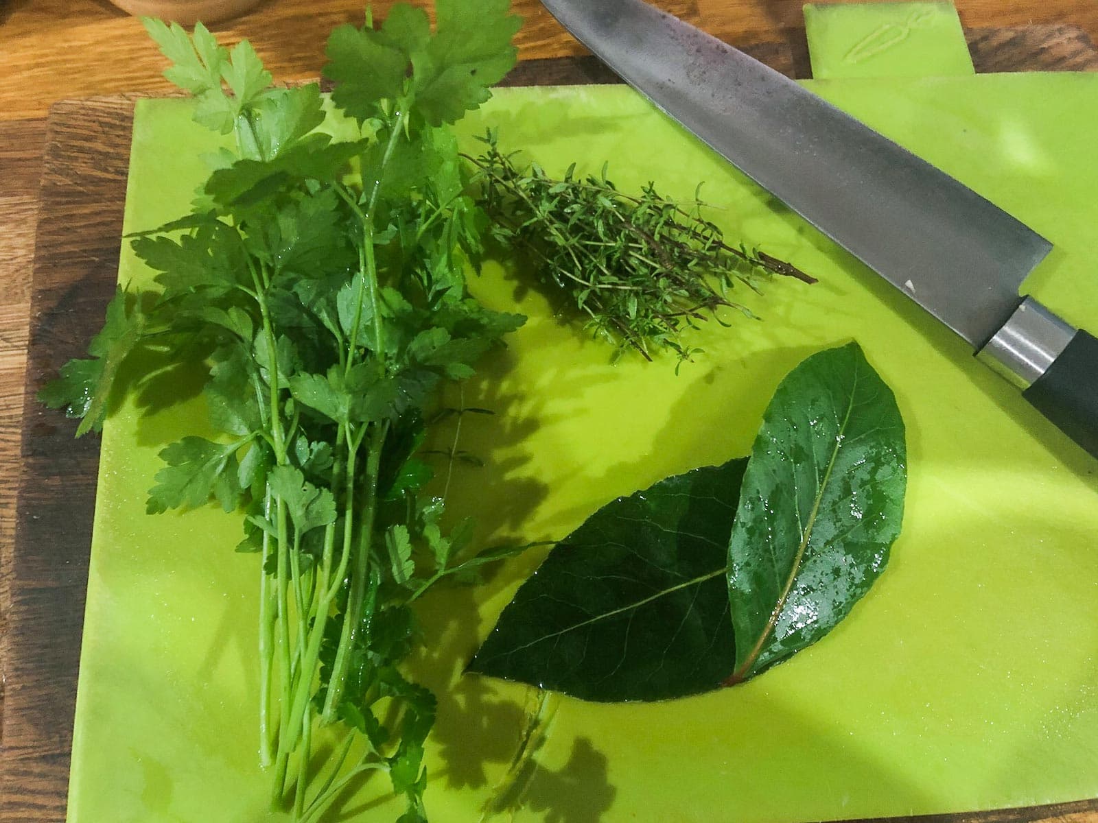 A green chopping board with a bunch of parsley, thyme and bay leaves freshly washed from the garden.