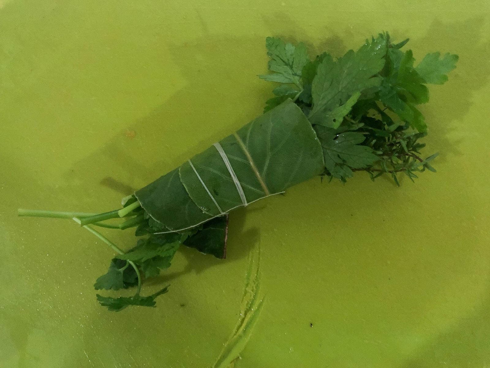 A green chopping board with a bouquet garni made of fresh herbs.