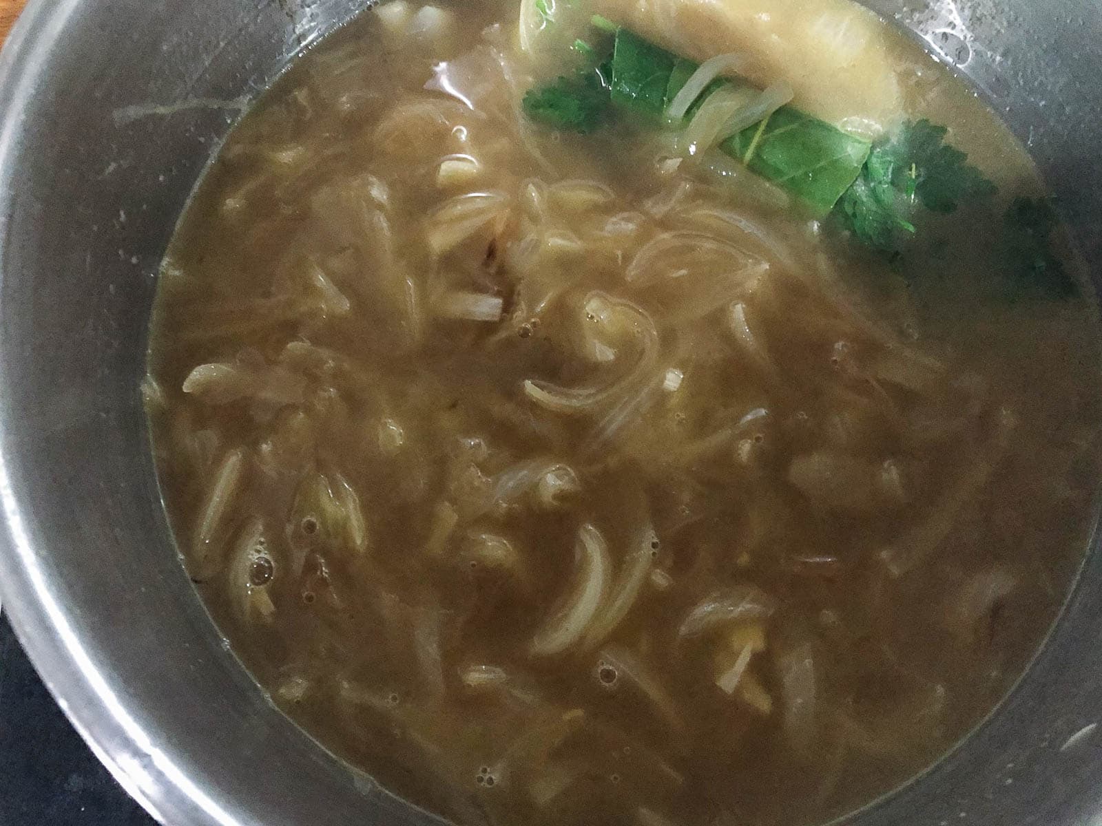 Sliced sautéed onions cooking in a beef broth with a fresh bouquet garni for making french onion soup.