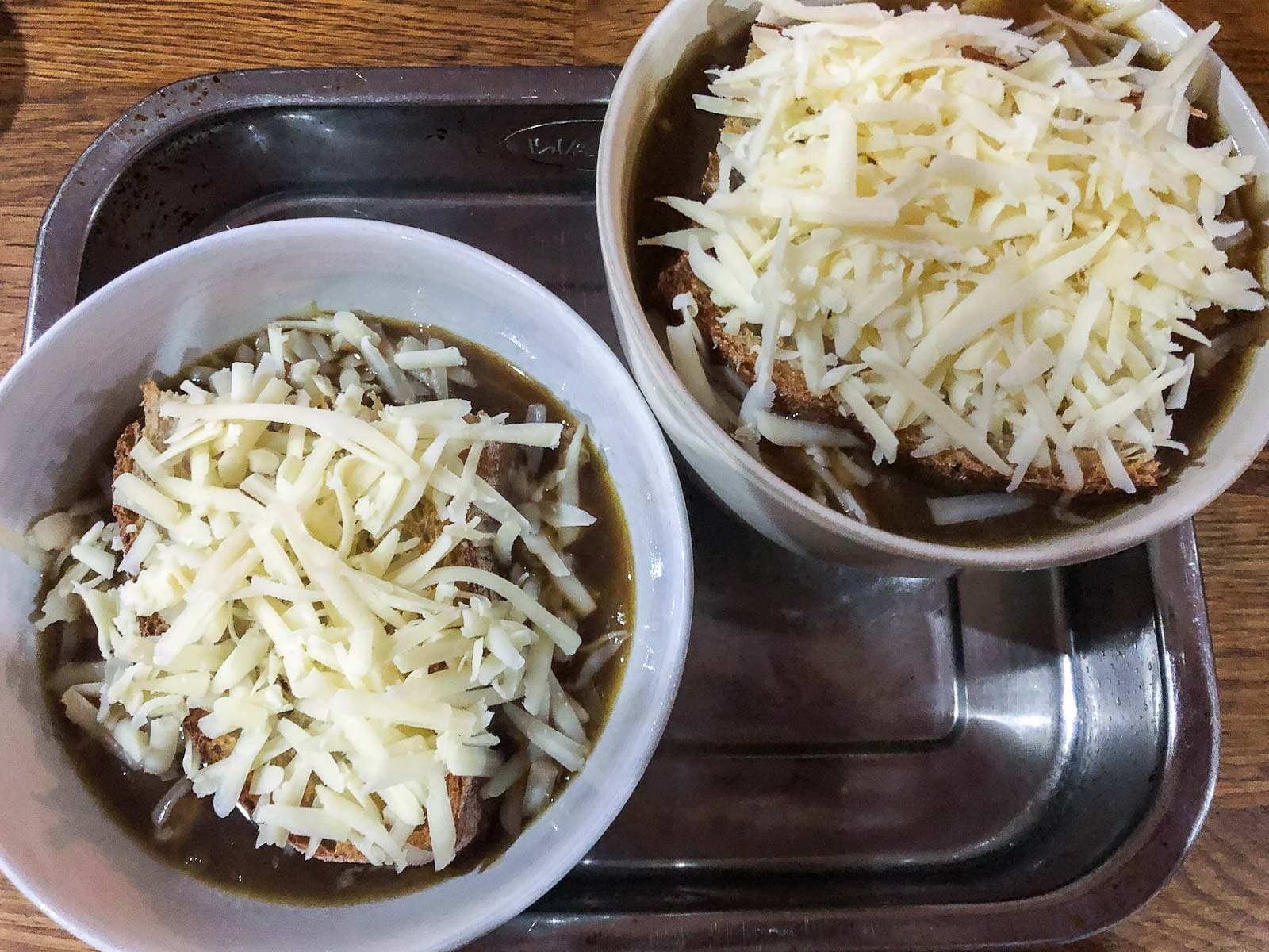 2 bowls of french onion soup topped with toasted bread and cheese ready to pop under the grill.