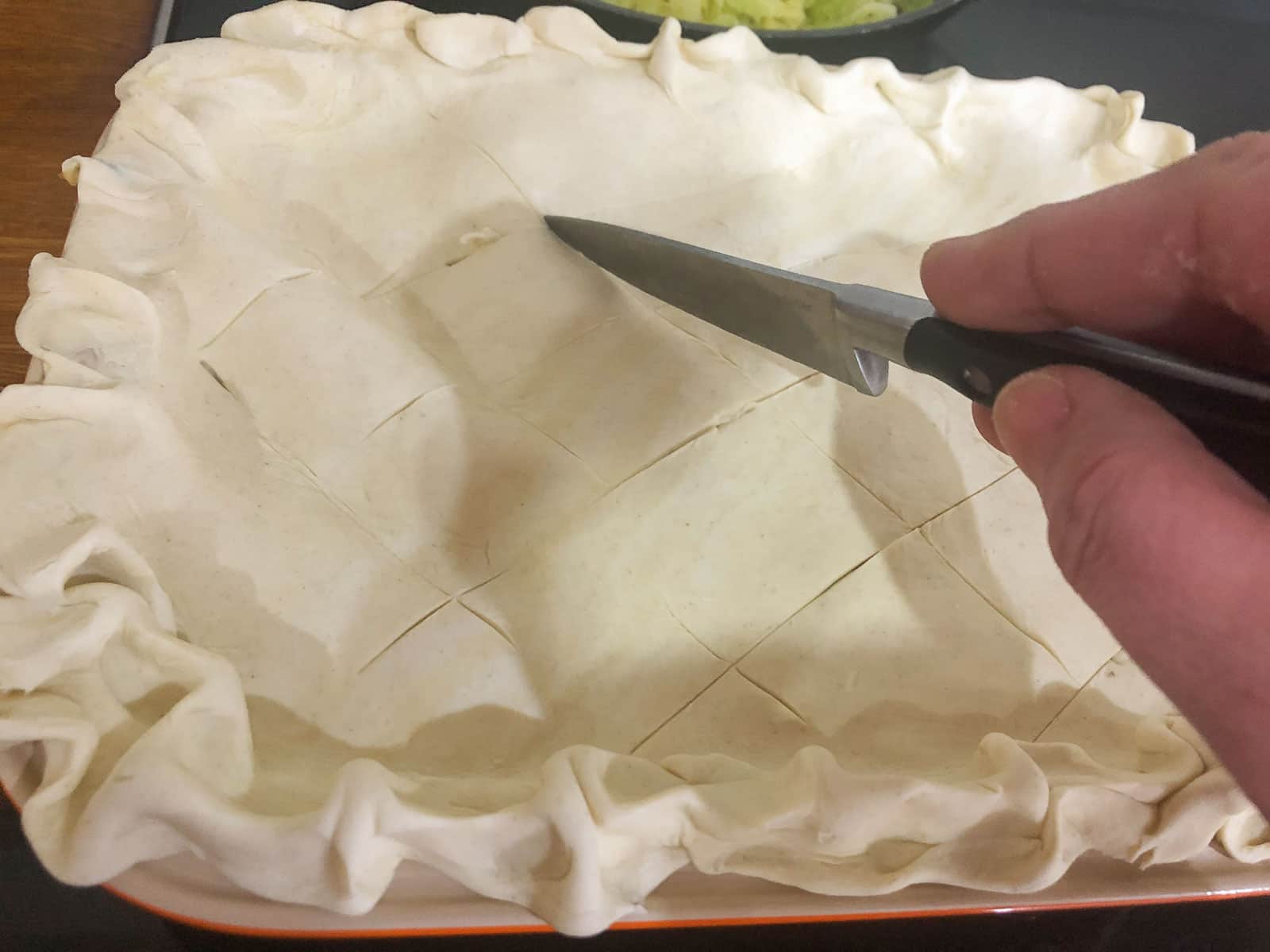 Scoring puff pastry on top of a turkey pie.