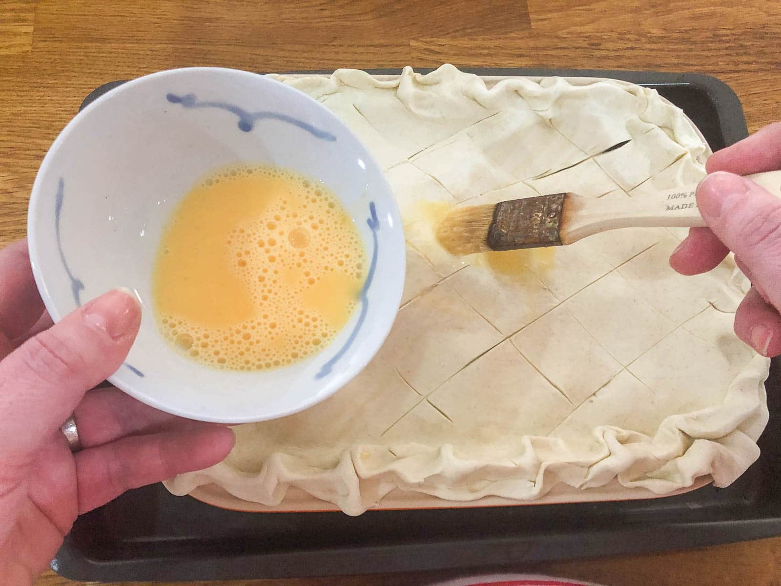 Adding a egg wash glaze to the top of the puff pastry of a turkey pie with a pastry brush before baking.
