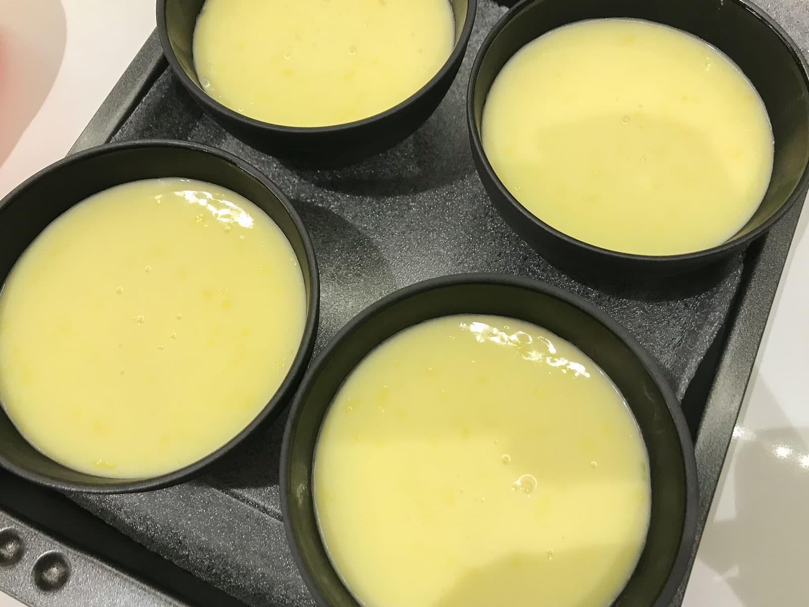 Lemon posset in small black bowls ready to be chilled.