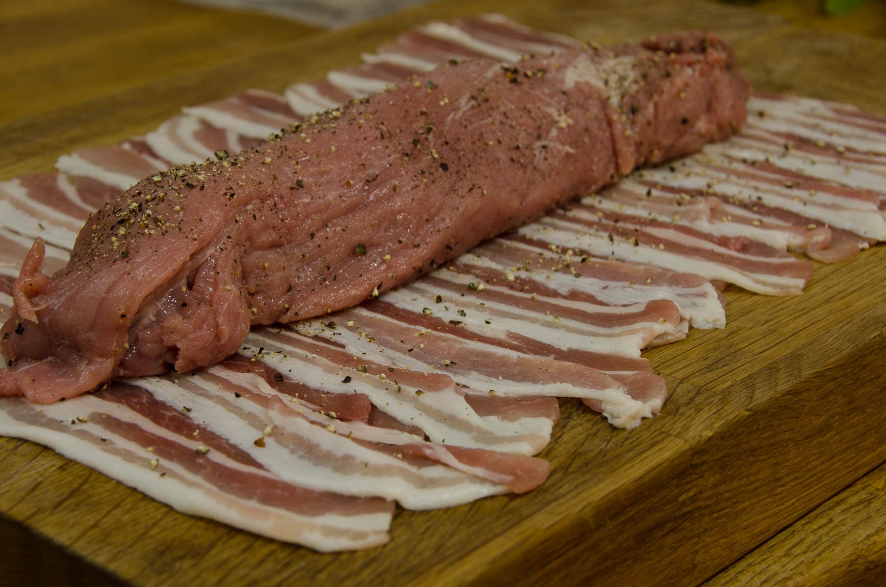 A layer of streaky bacon strips with a piece of seasoned pork fillet on top .