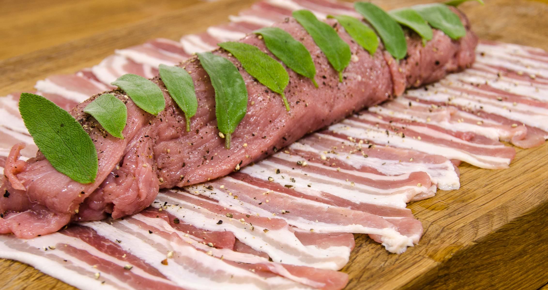 A layer of bacon strips topped with seasoned pork fillet and sage leaves.