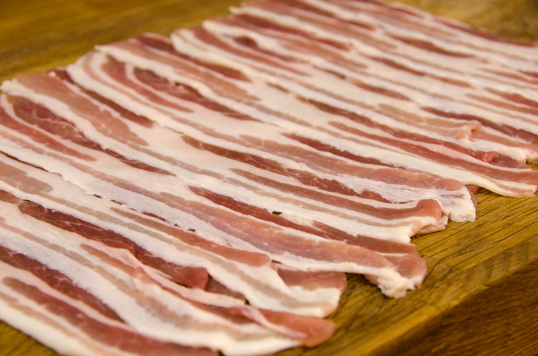 Strips of smoked streaky bacon on a wooden board.
