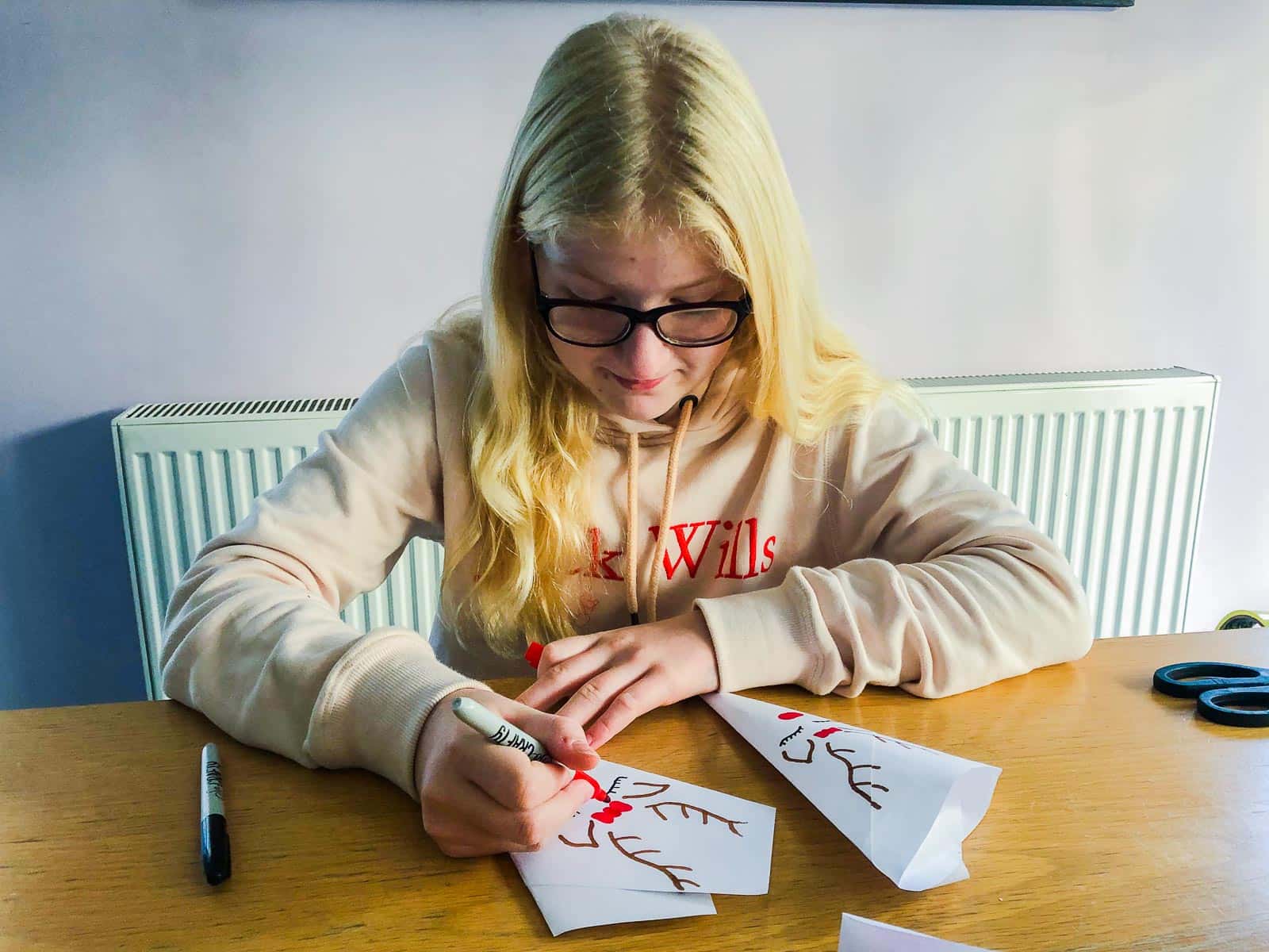 A young girl drawing reindeer faces on paper cones.
