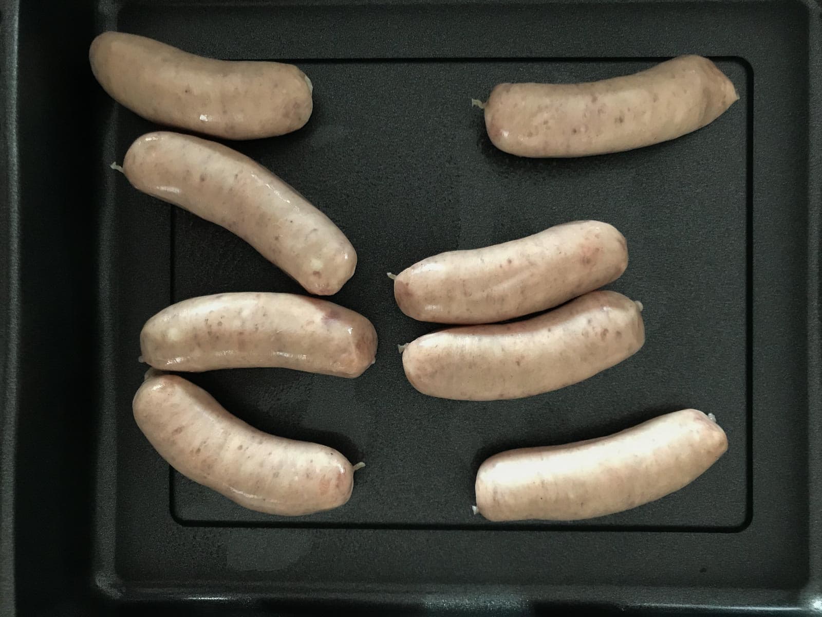 8 plain pork sausages on a black metal roasting tray.