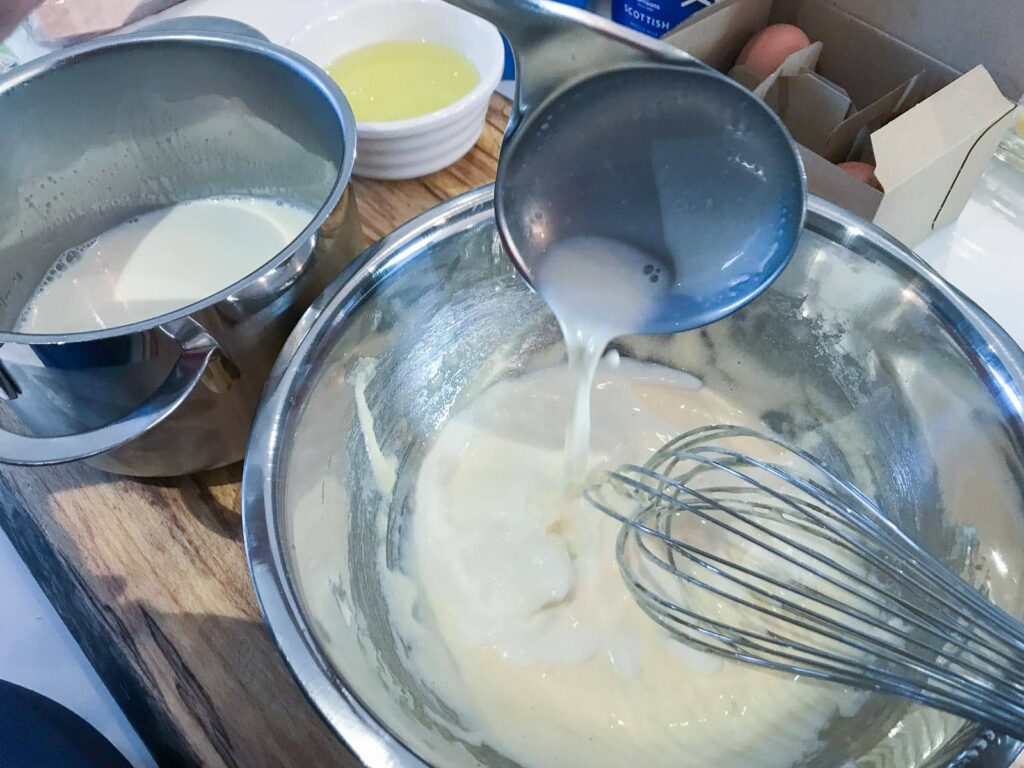 A ladle of hot milk being added to eggs and sugar to make a custard.