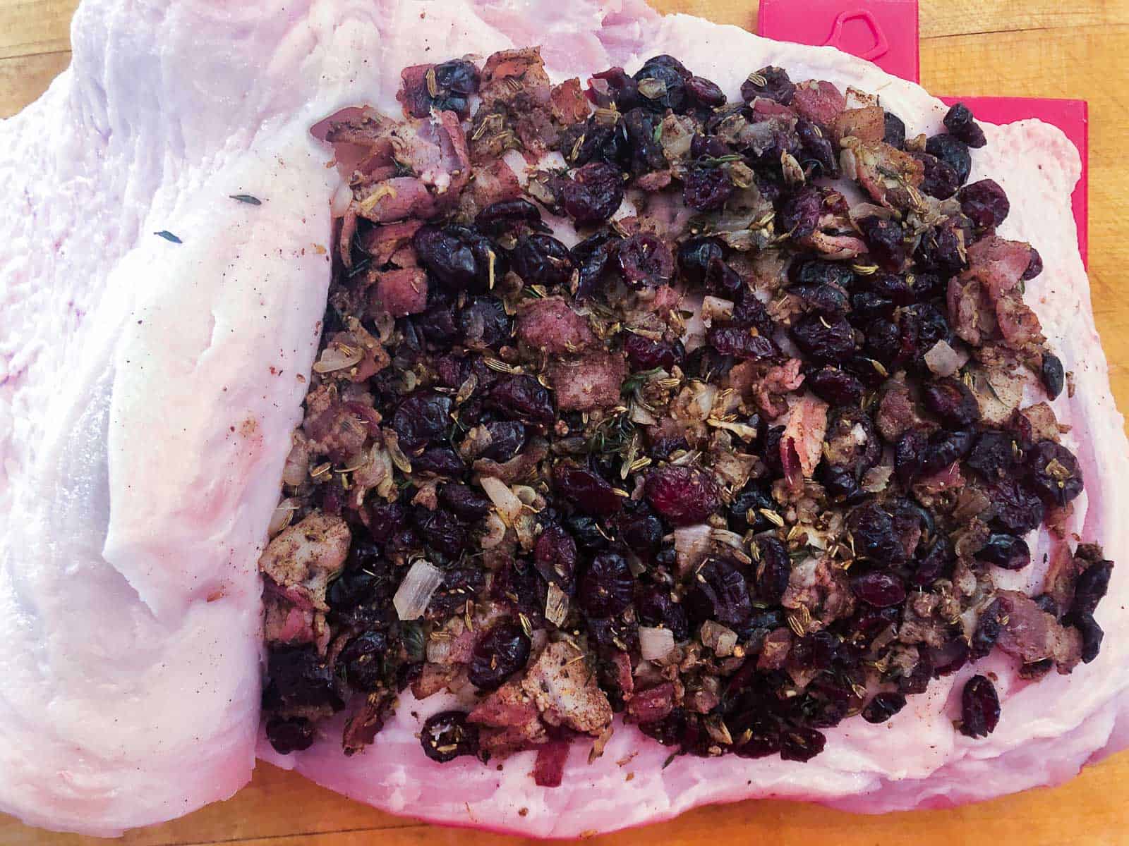 Adding a cranberries spiced stuffing to a pork roast before tying it for cooking.