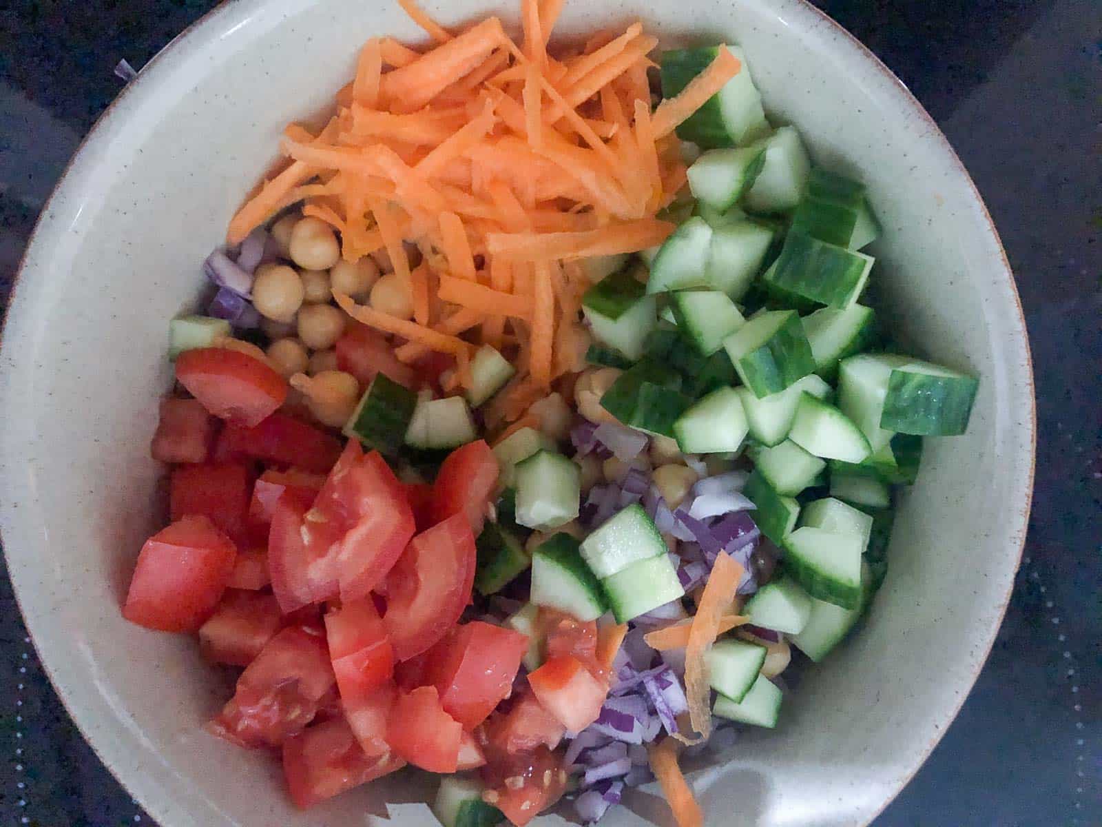 Diced tomatoes, cucumber, grated carrot, chickpeas and red onion in a bowl.