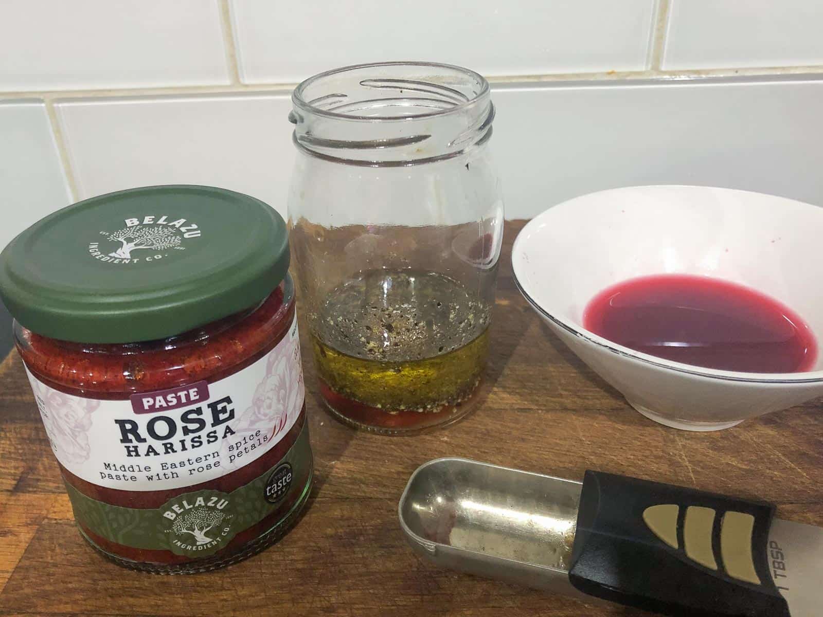 A jar of Belazu Rose Harissa paste and a jar of homemade salad dressing.