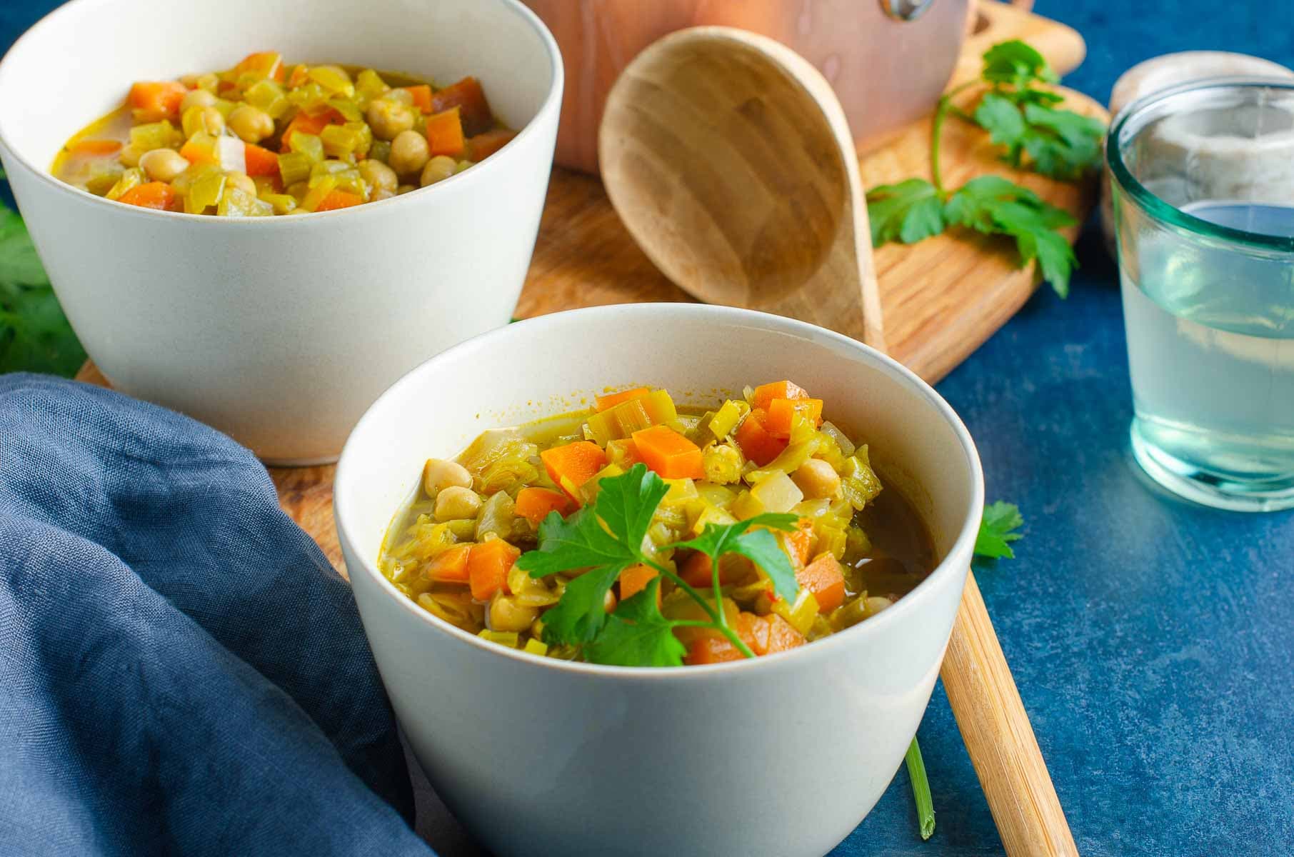 2 bowls of curried chickpea and vegetable soup on a blue background