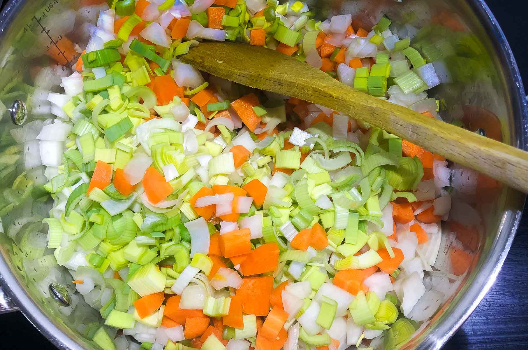 Onions, leeks and carrots diced in a frying pan sauteeing.