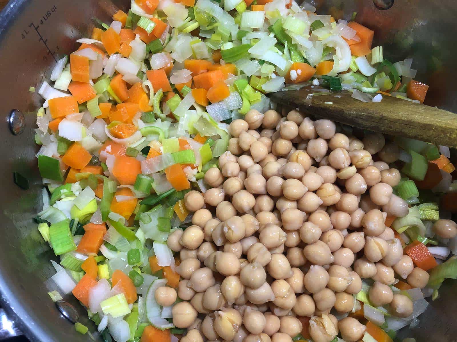 A tin of chickpeas drained and added to sauteed vegetables in a frying pan.