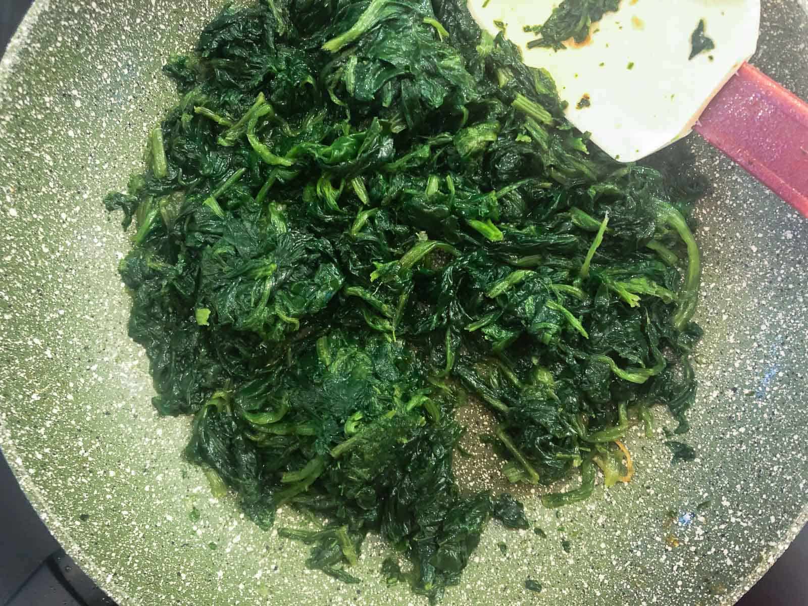 Spinach cooking in a green coloured fry pan.