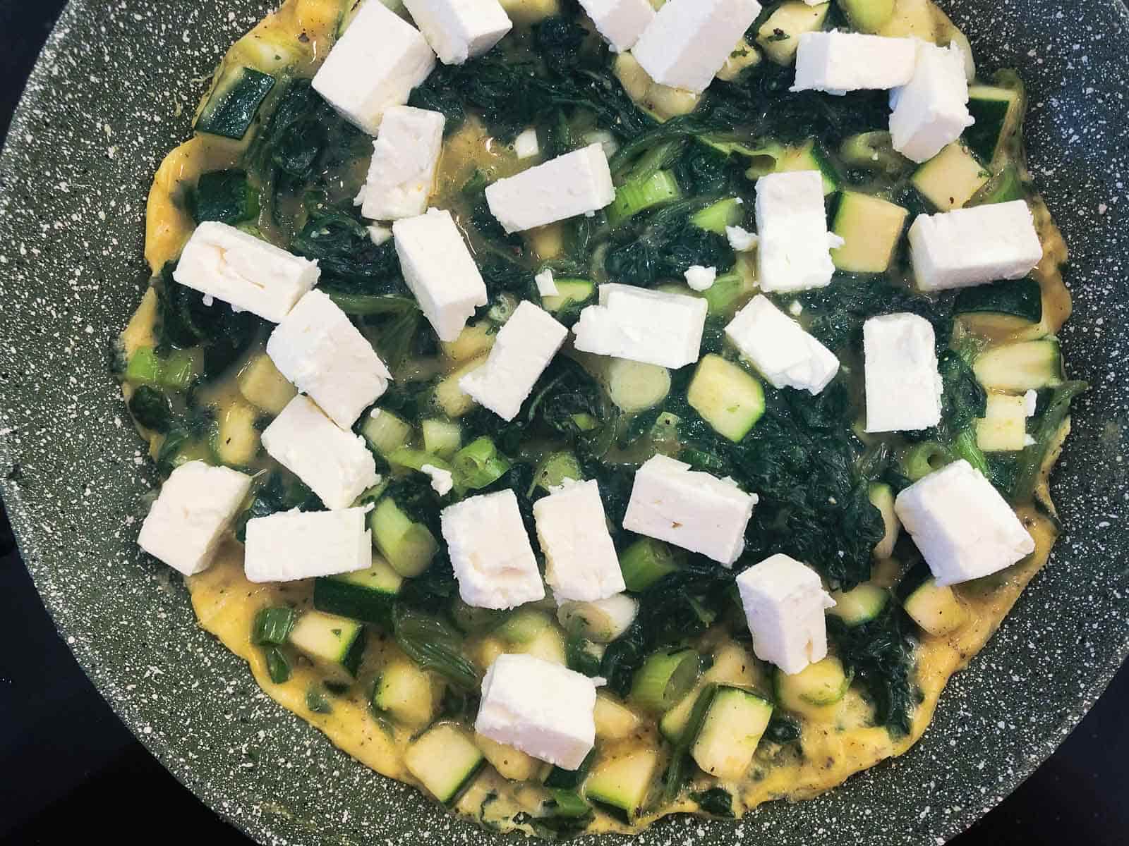 An omelette filled with green vegetables and topped with feta cheese ready to pop under the grill.