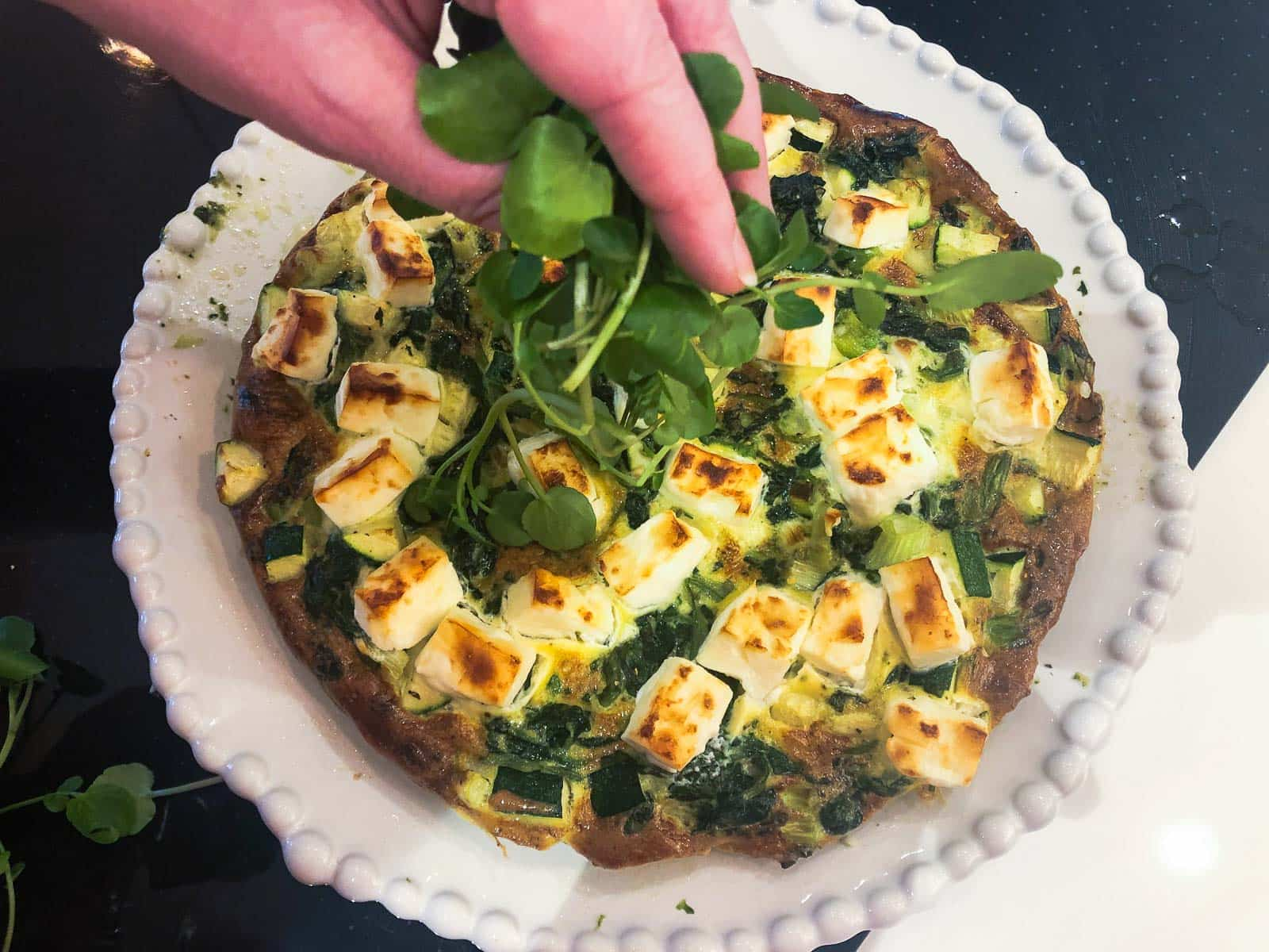 Adding fresh watercress to the top of a cooked spinach omelette.