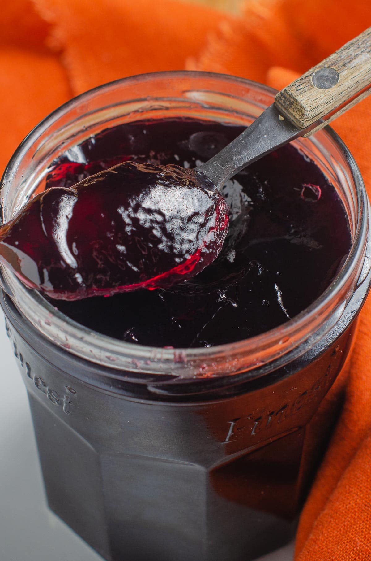 A jar of blackcurrant smooth jelly with a wooden handle spoon.