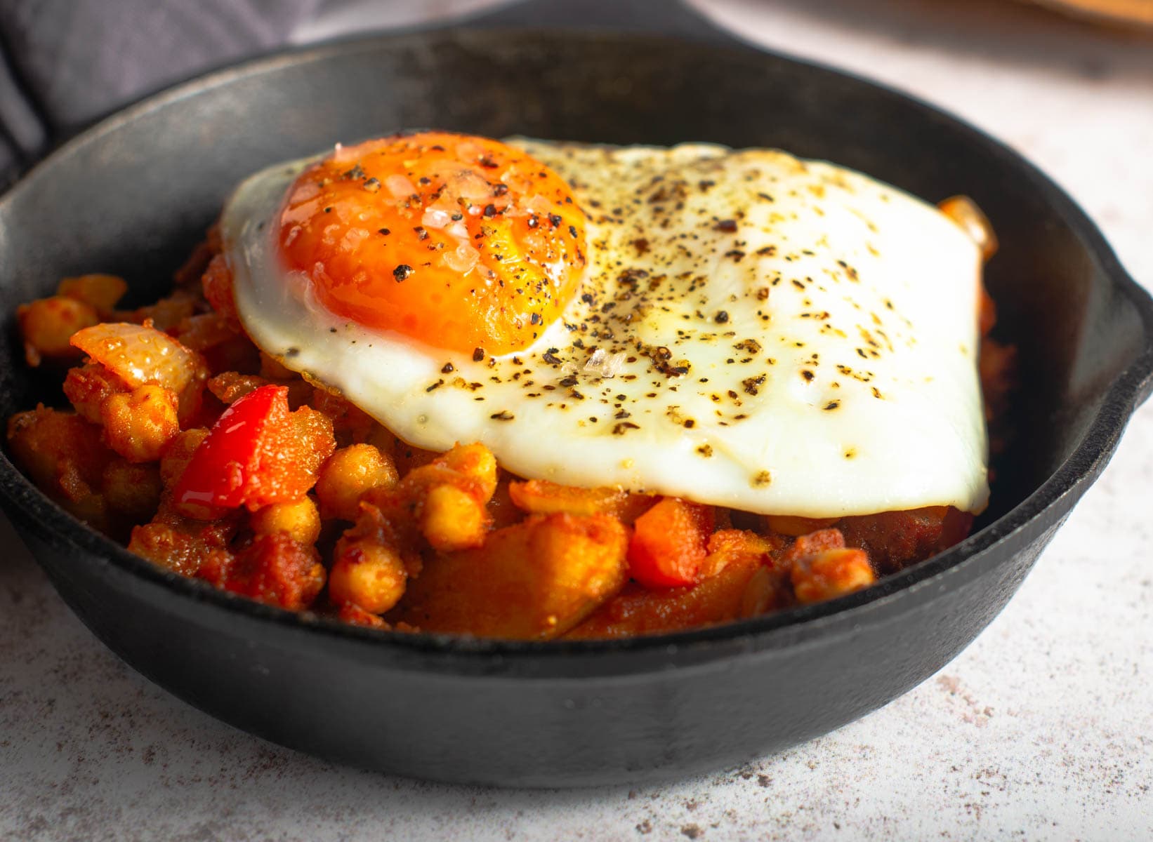 A finished brunch dish using leftover potatoes, chorizo and spices served in a small cast iron fry pan and topped with a runny fried egg.