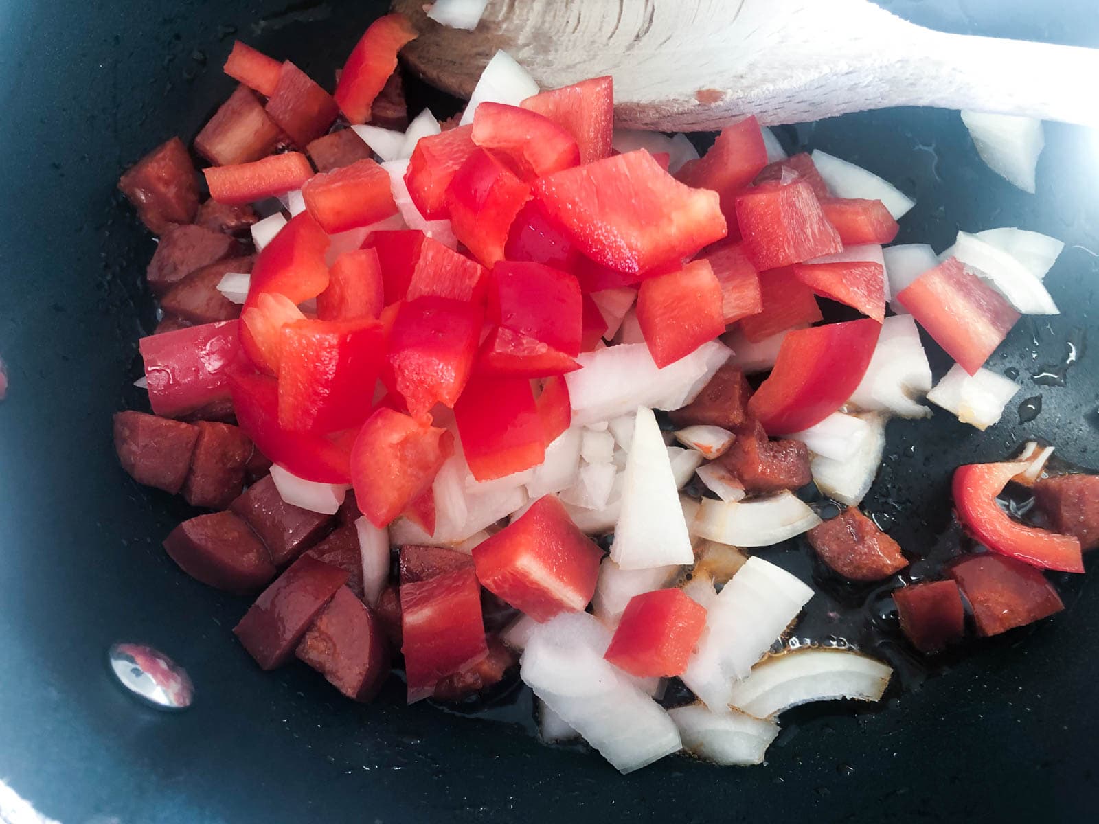 diced chorizo, onions and red peppers sauteeing in a frying pan.