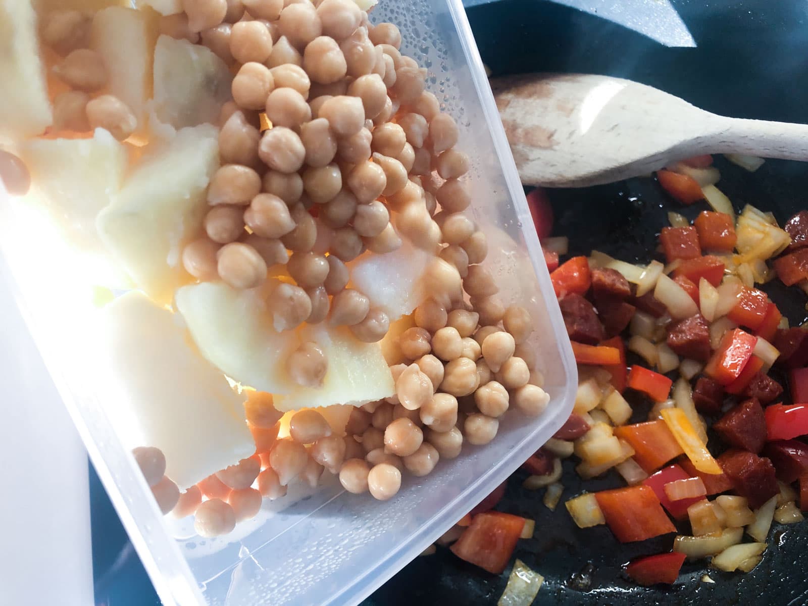 Chickpeas and leftover cubed potatoes being added to sautéed vegetables in a fry pan.