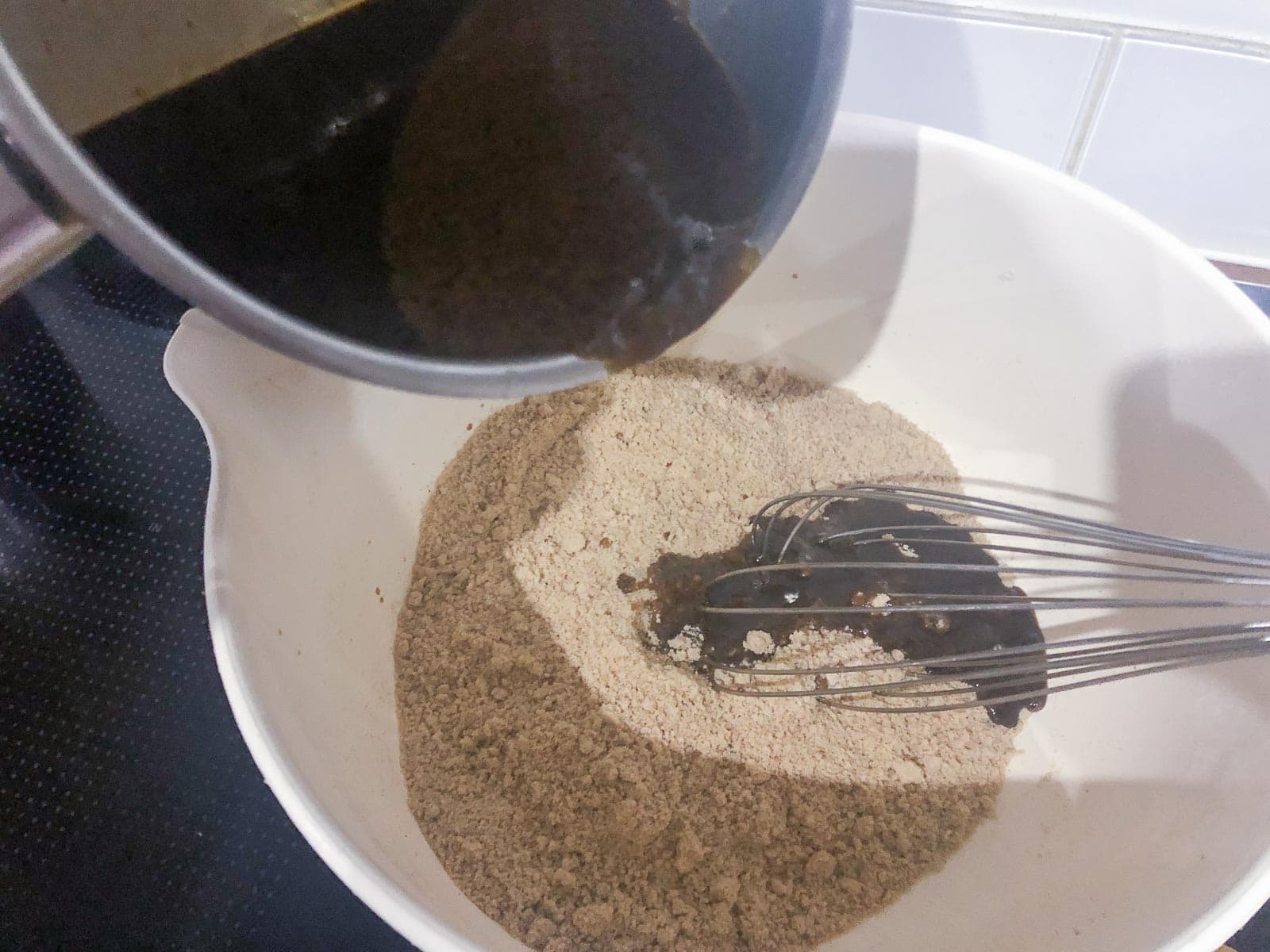 pouring warm melted sugars and syrups into flour and butter mixture