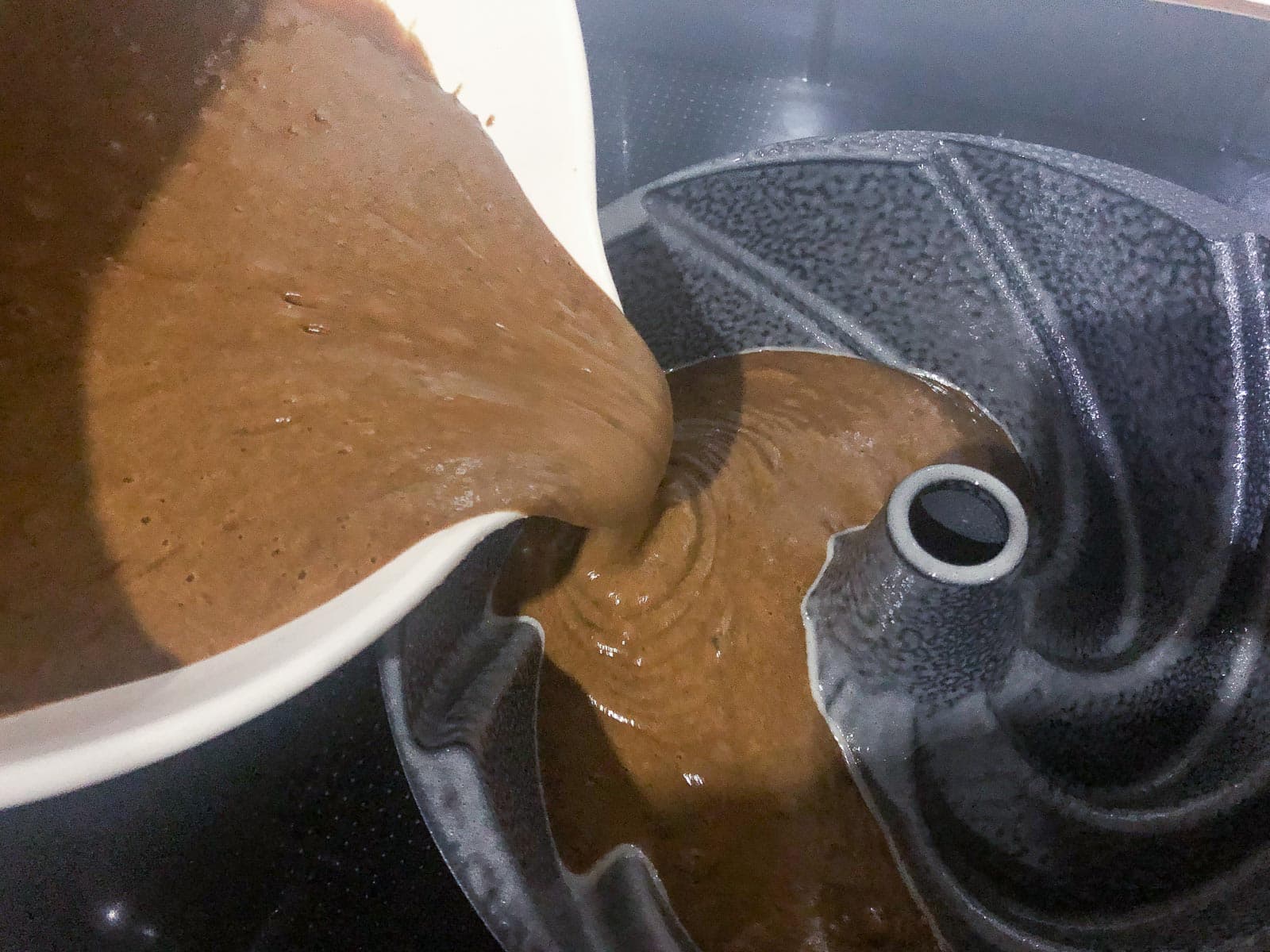 pouring a gingerbread cake batter into a well greased bundt tin.