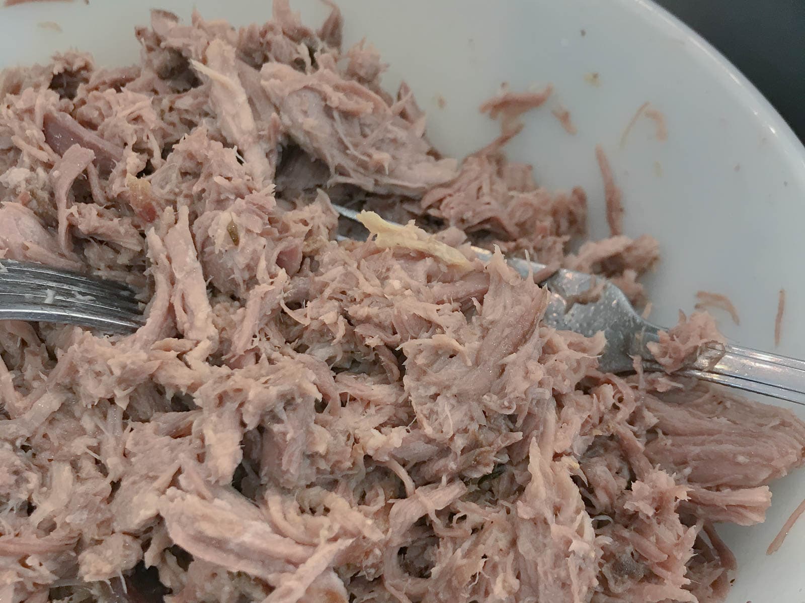 a bowl of juicy pulled pork with 2 forks in the dish