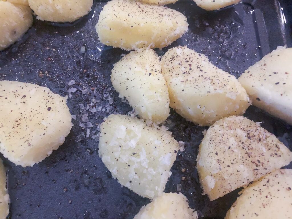 Potatoes in a roasting tray ready to roast well seasoned with sea salt and black pepper.