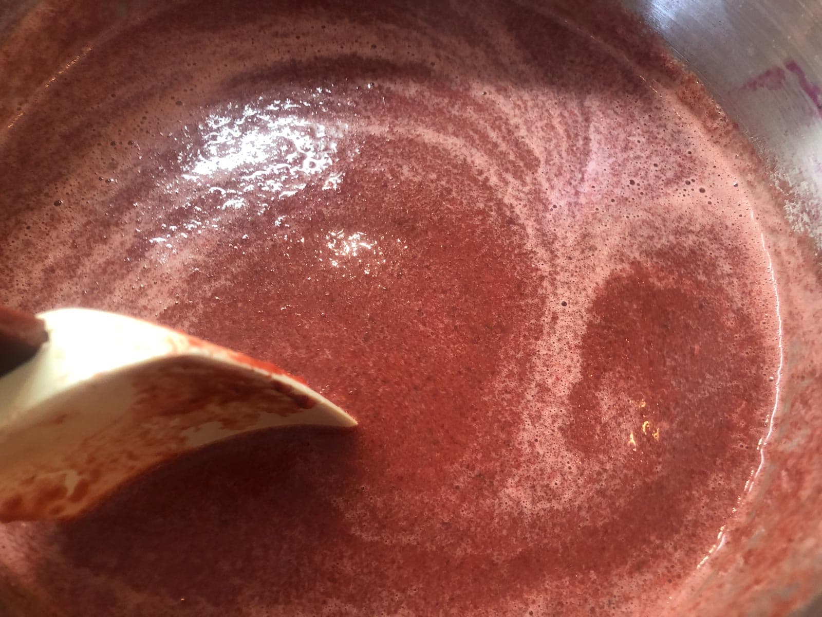 Creamy thai beetroot soup in the final stages in a pan being stirred.