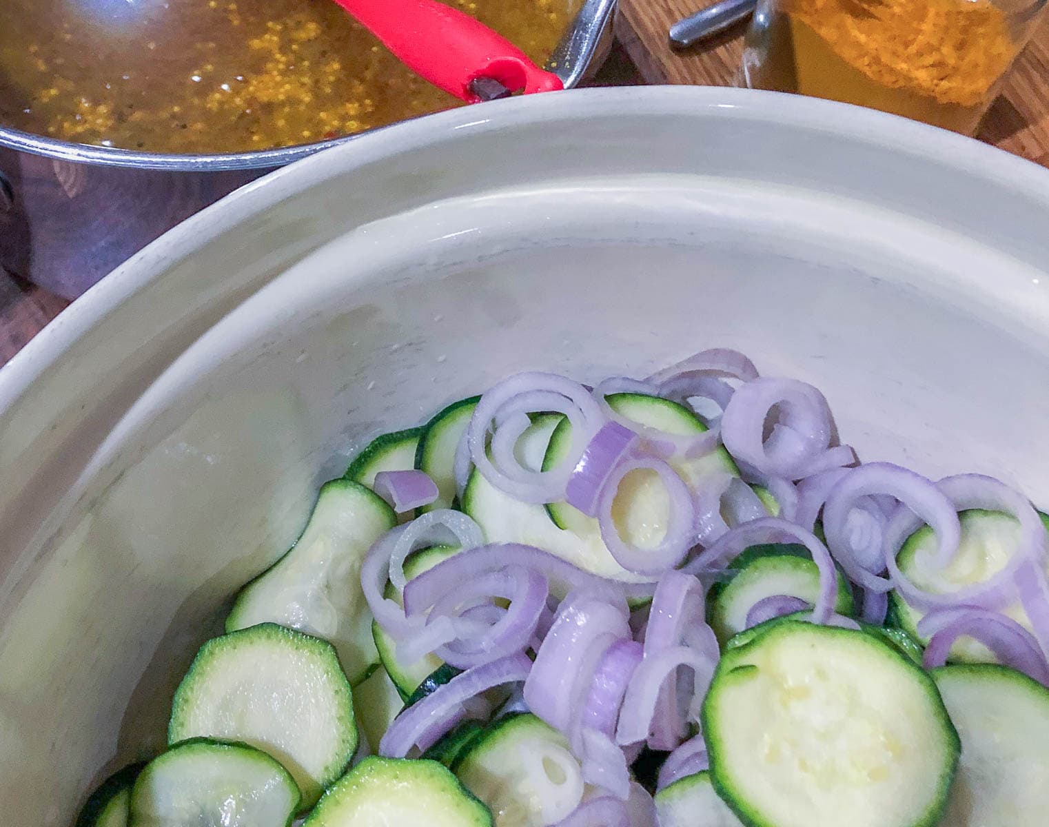 sliced courgettes and shallots in a bowl with a mustard vinegar sauce to the back in a pan.