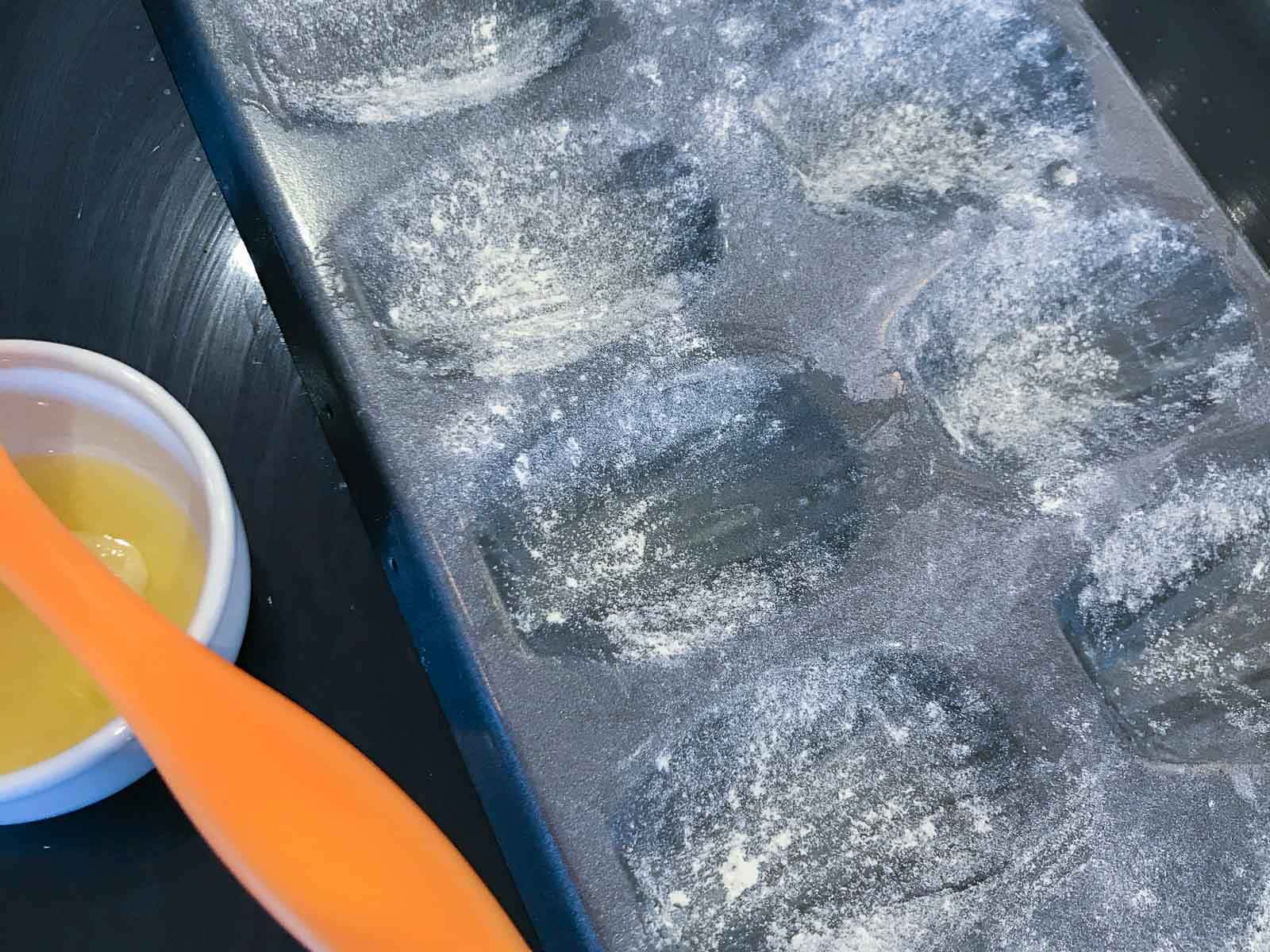 a well floured madeleine tray and a dish with melted butter and silicone pastry brush