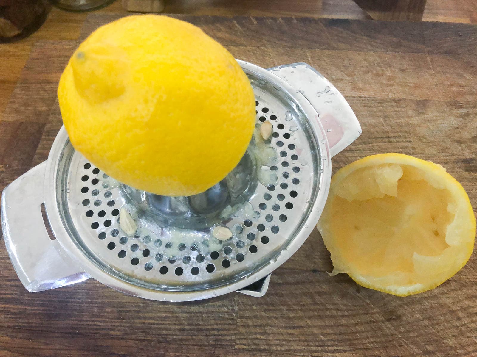 Lemon juiced on a metal juicer sitting on a wooden chopping board.
