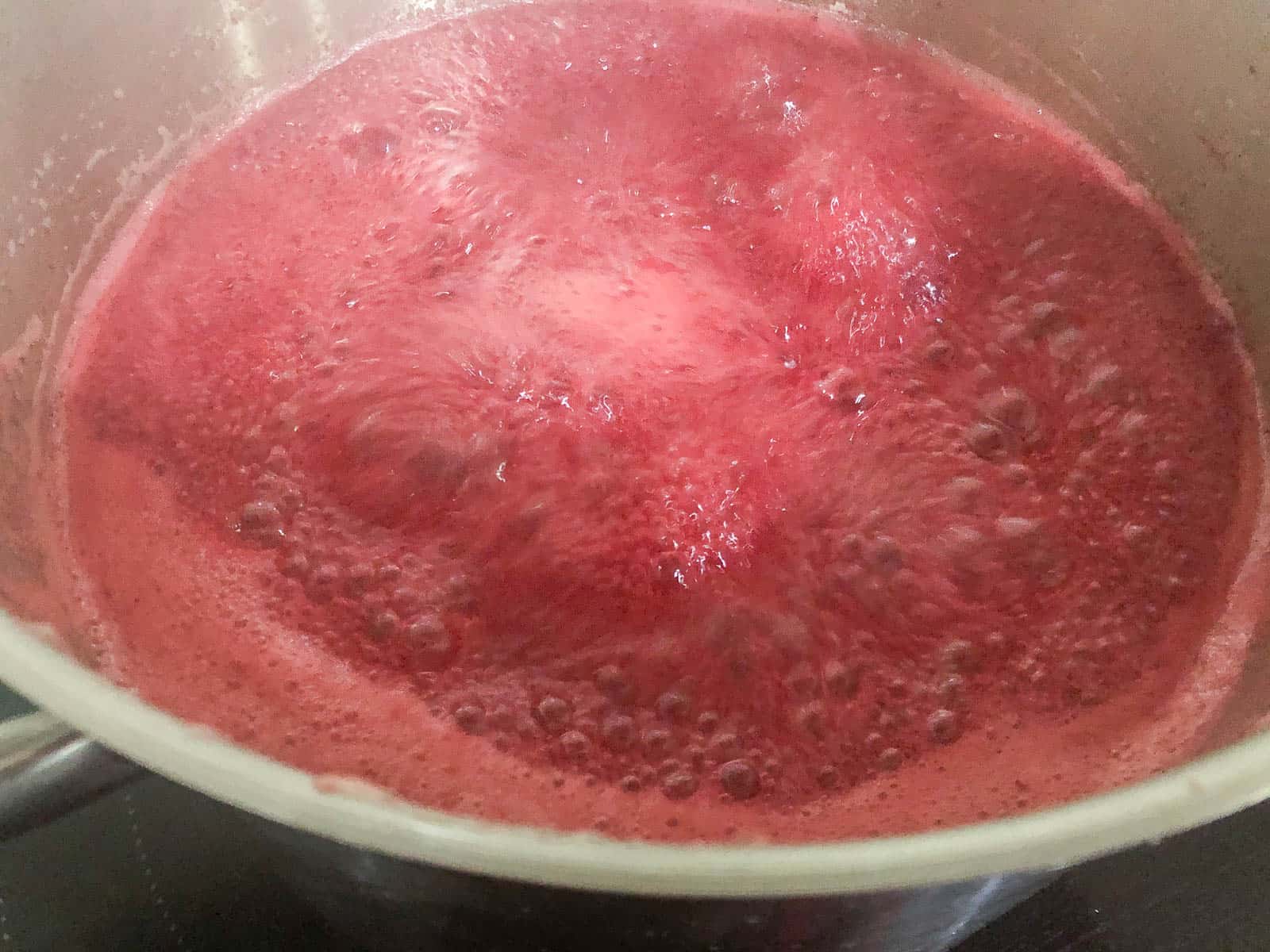 Raspberry jam at the rolling boil stage of jam making process.